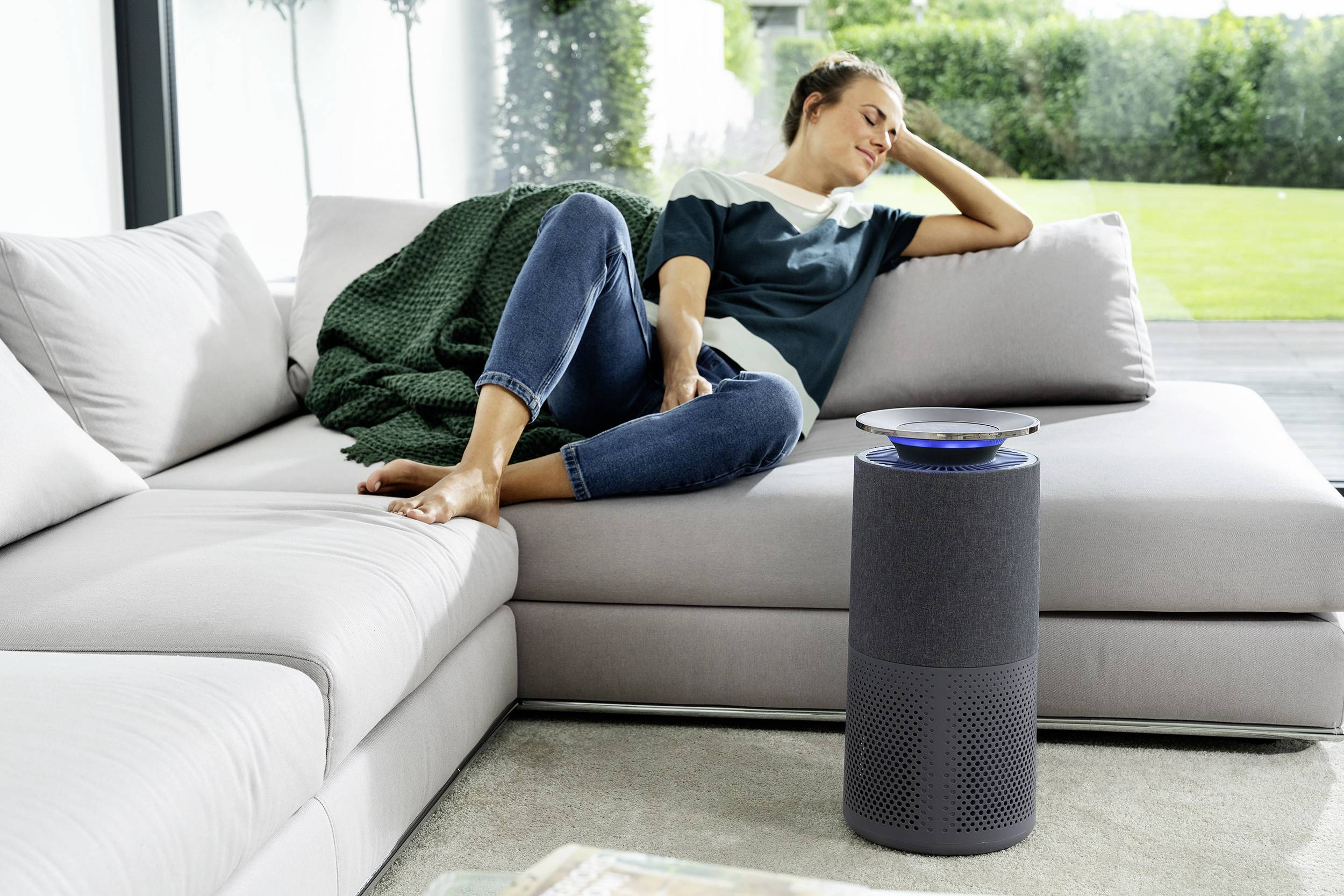 Une personne se détend sur un canapé dans un salon à côté d'un haut-parleur intelligent.