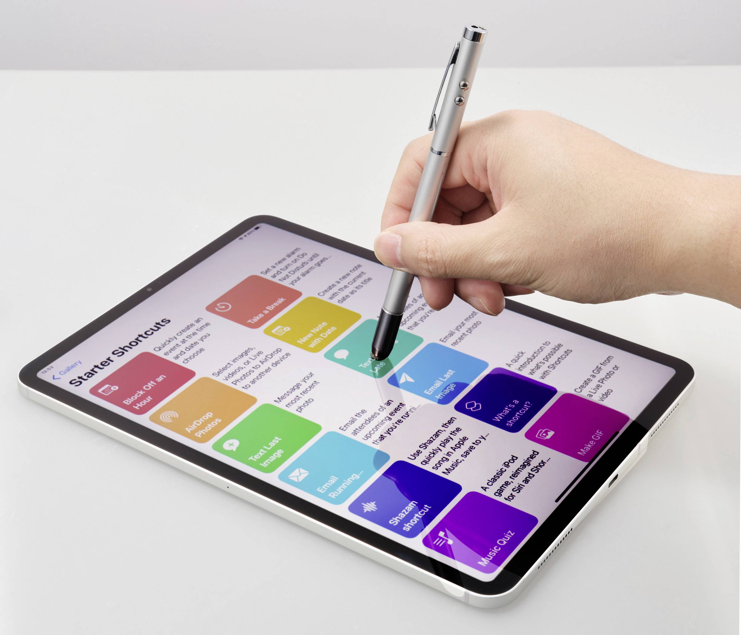Une main manipule un stylet sur une tablette pour toucher des raccourcis d'applications colorés sur un écran. Différentes applications sont visibles.