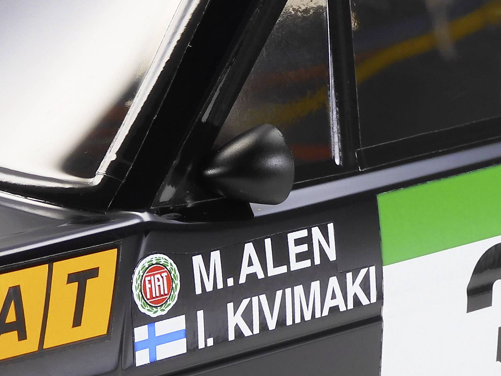 Gros plan d'une voiture de rallye portant les noms 'M. Alen' et 'I. Kivimaki' sur la portière, à côté d'un logo Fiat. Le drapeau finlandais est visible.
