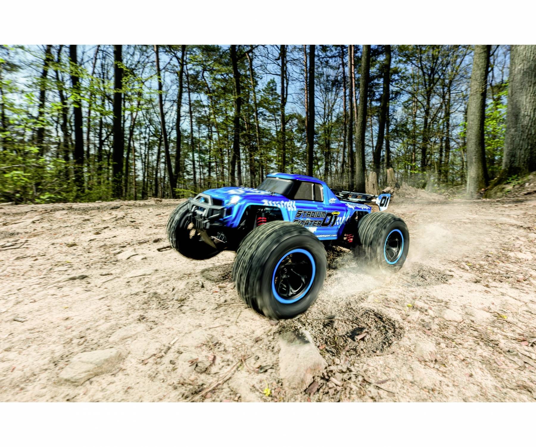Une voiture tout-terrain bleue télécommandée roule à grande vitesse sur une surface forestière rocheuse et poussiéreuse.