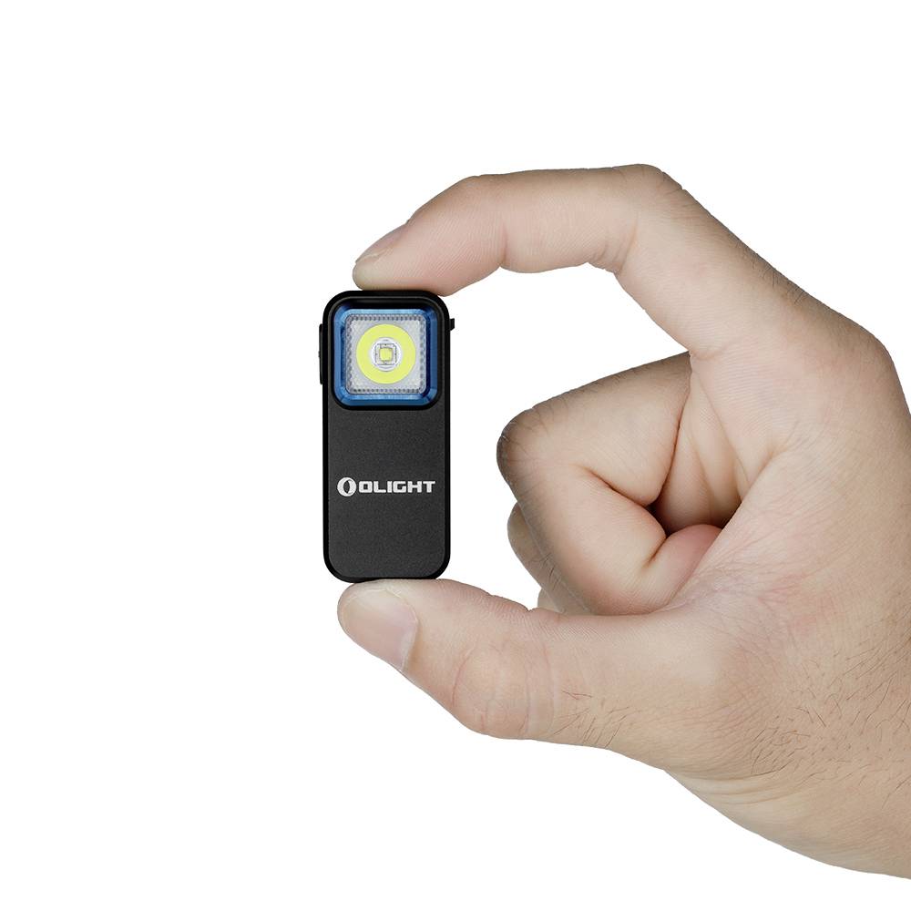 Une main tient une petite lampe de poche rectangulaire avec l'inscription 'OLIGHT' sur la face avant.