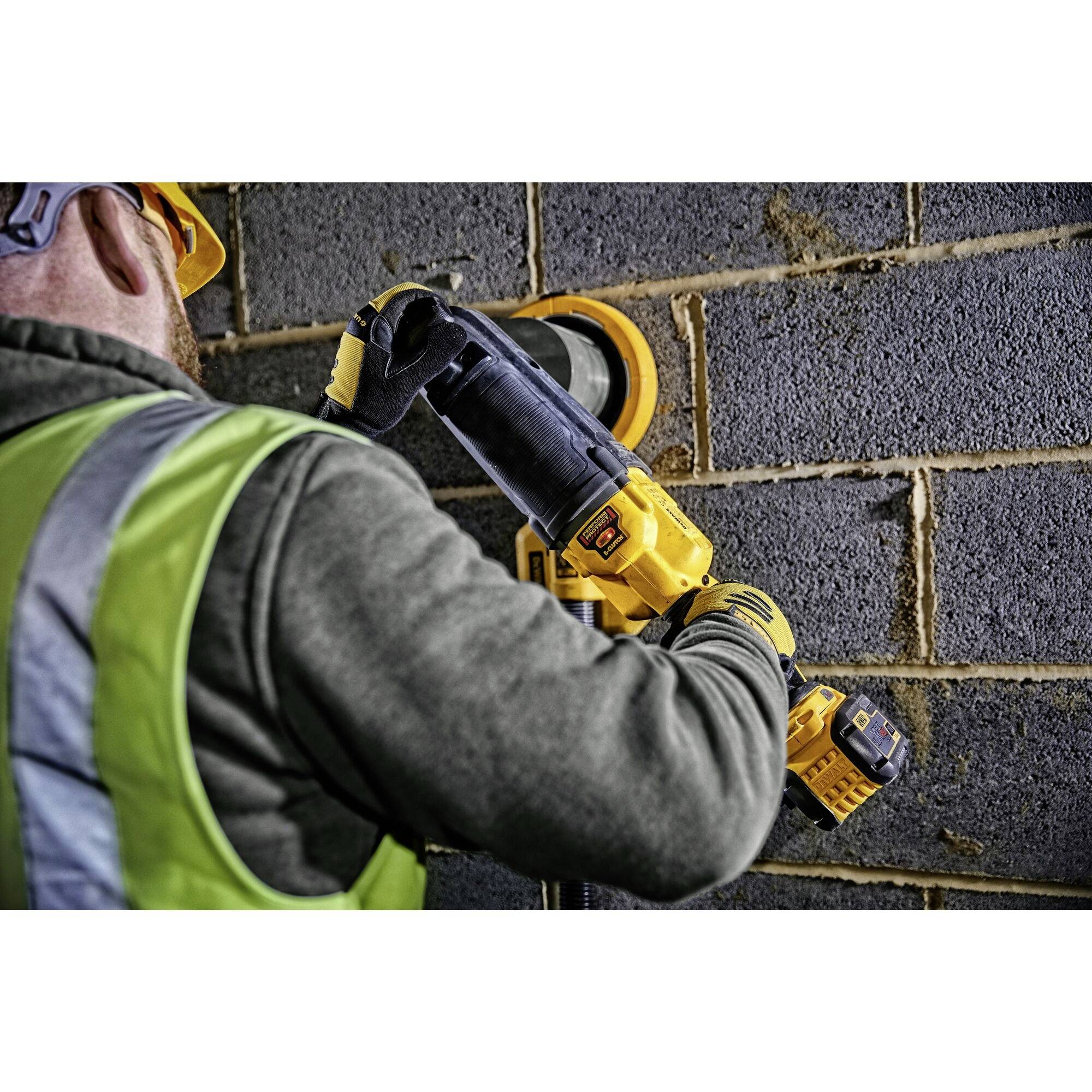Un ouvrier porte des vêtements de protection et utilise une scie électrique sur un mur de briques.
