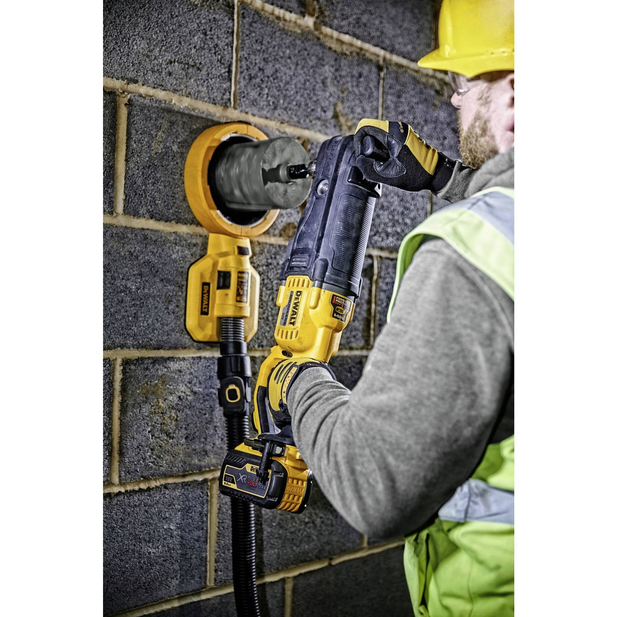 Une personne portant un gilet de protection et un casque fore un trou rond dans un mur de briques à l'aide d'un outil électrique.