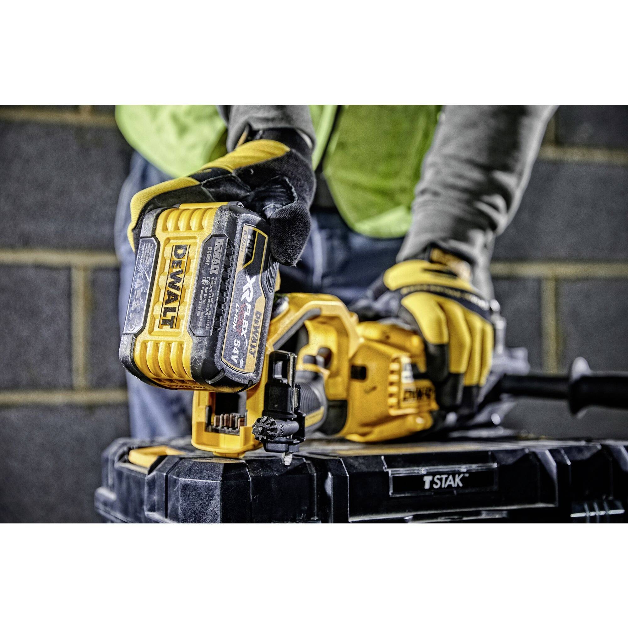 Une personne porte des gants jaunes et utilise un outil sans fil DeWalt.