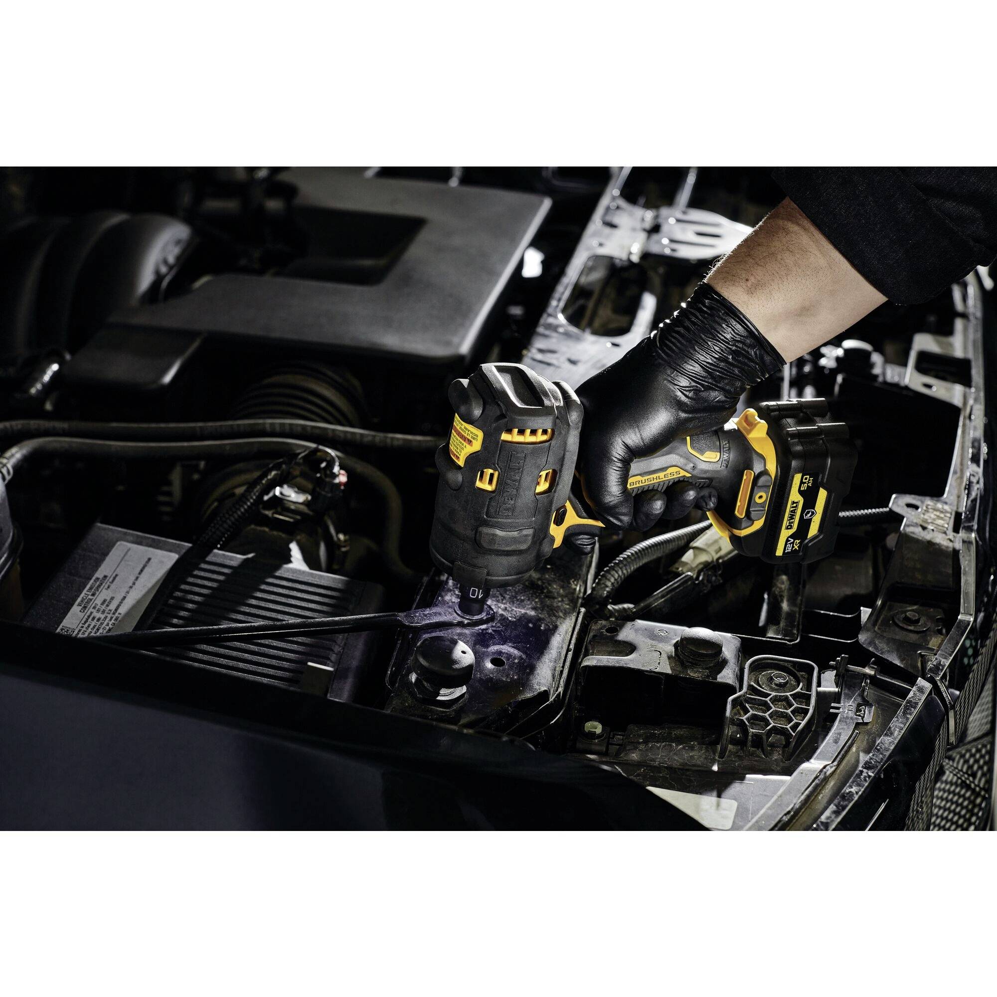 Un mécanicien utilise une visseuse à choc sans fil pour travailler sur un moteur de voiture. Le compartiment moteur est partiellement visible.