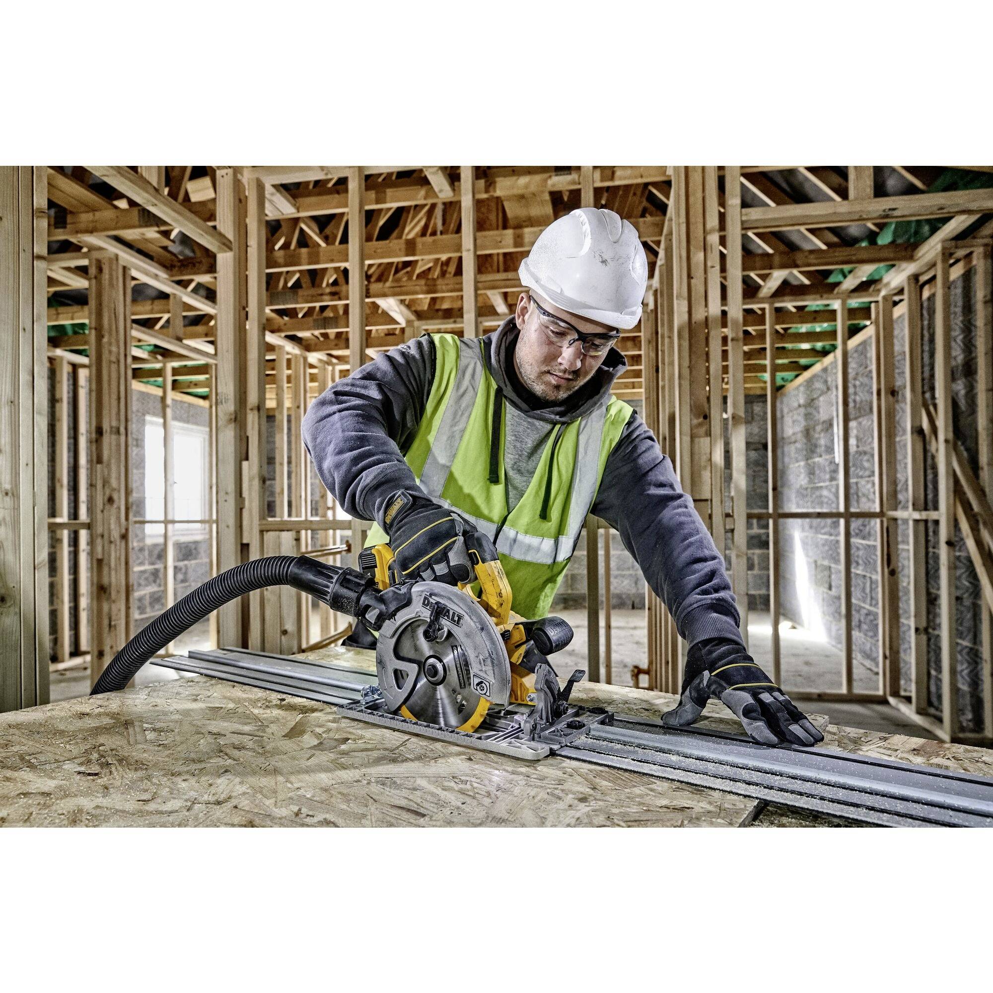 Un ouvrier portant un casque et des lunettes de protection coupe du bois à la scie circulaire dans un bâtiment en cours de construction.