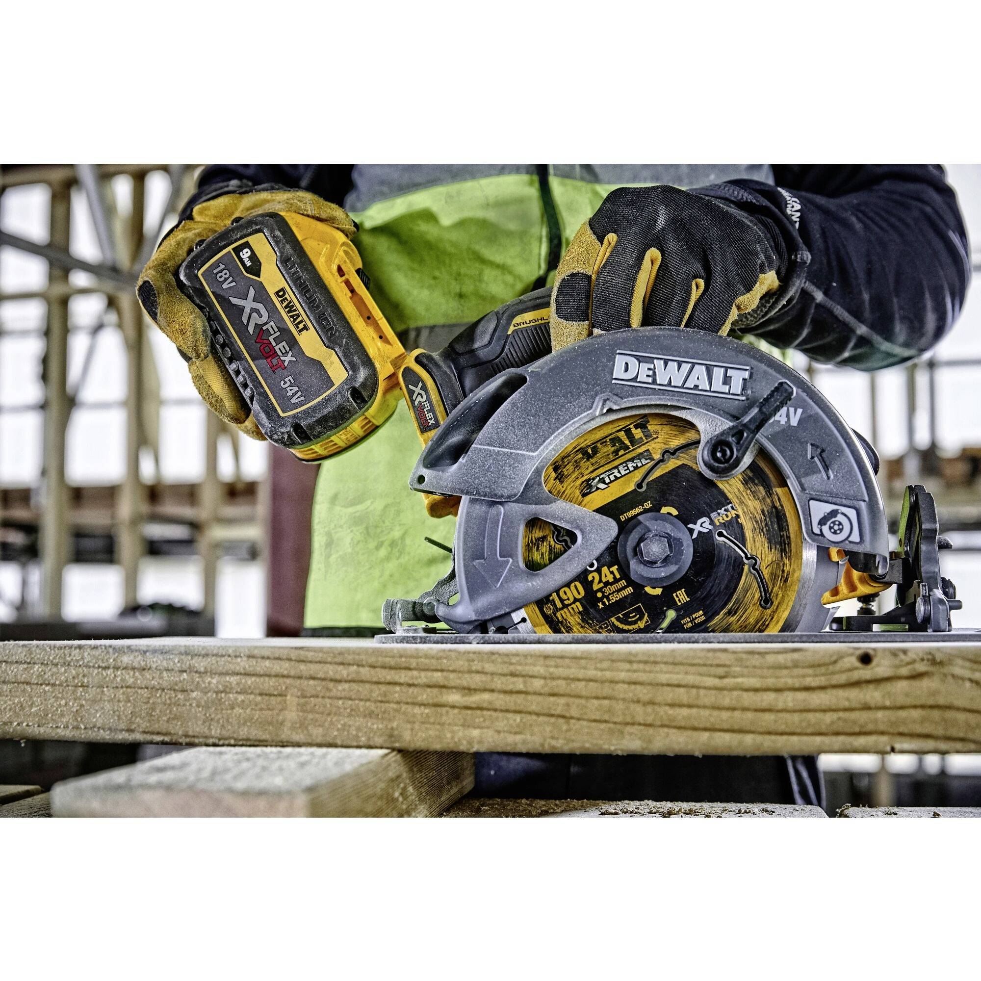 Une personne porte des gants et utilise une scie circulaire sans fil DeWalt pour couper une planche en bois. Un échafaudage est visible en arrière-plan.