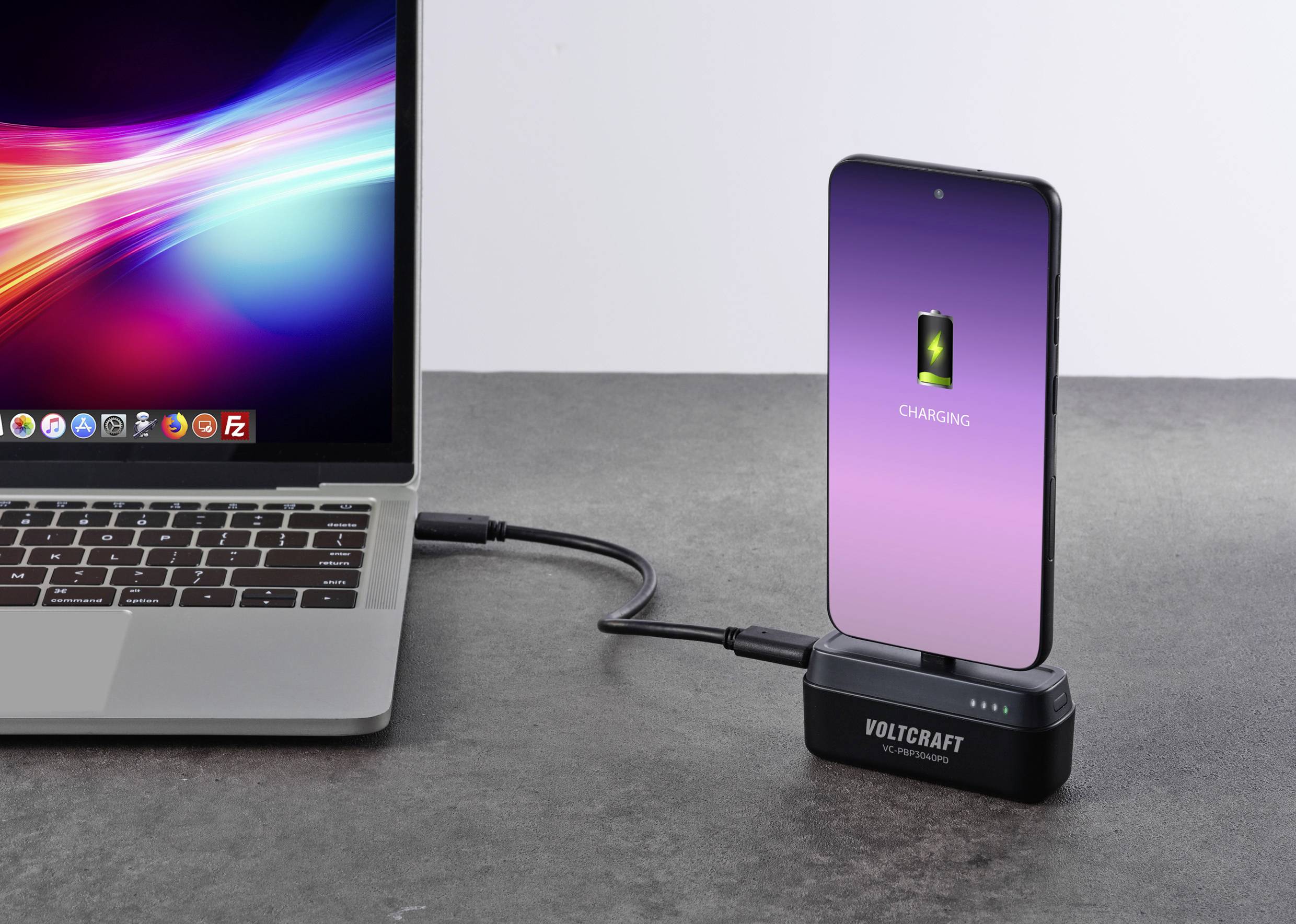 Un smartphone est en charge via un câble connecté à un ordinateur portable. L'écran du smartphone affiche un symbole de chargement.