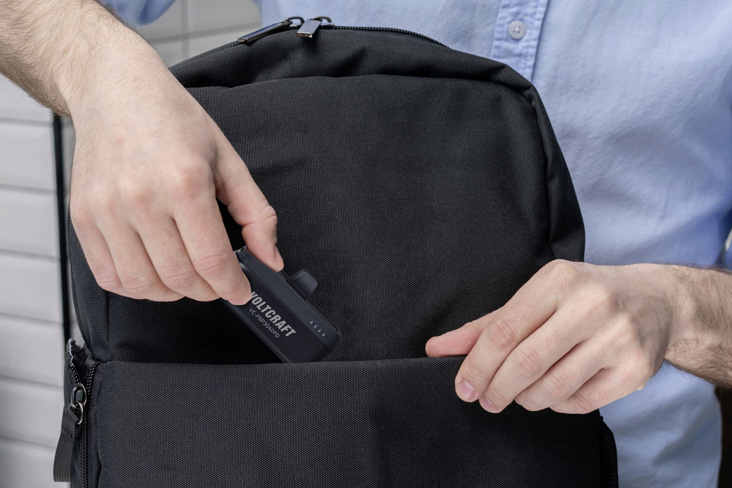 Une personne range un ensemble d'outils dans un sac à dos noir. La personne porte une chemise bleu clair.