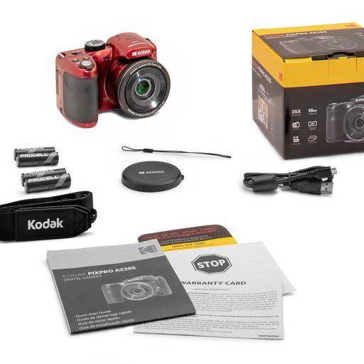Appareil photo numérique rouge avec accessoires : batteries, chargeur, bouchon d'objectif, bandoulière et mode d'emploi à côté de son emballage.