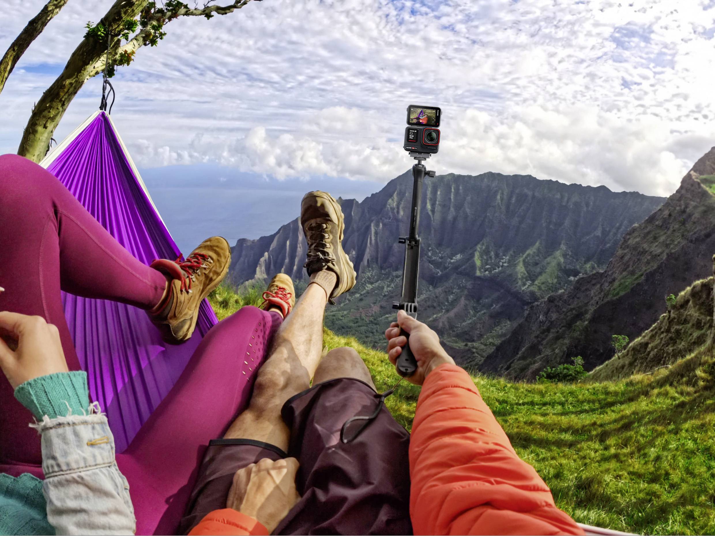 Des personnes se détendent dans un hamac avec une vue sur les montagnes. Une personne tient un appareil photo pour capturer le panorama.