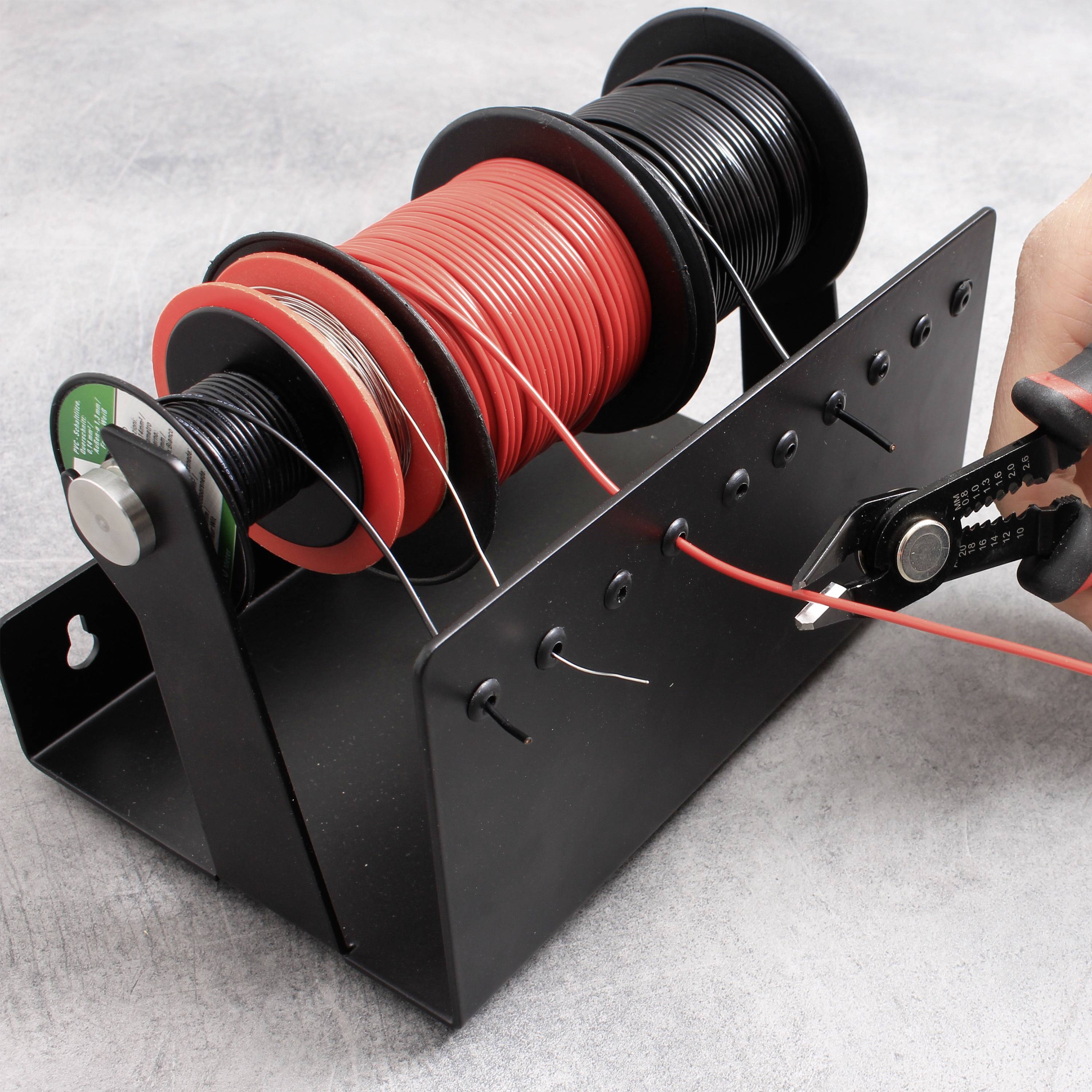 Bobine avec des câbles rouges et noirs sur un support. Une main retire un câble rouge. Environnement de travail avec un fond gris.