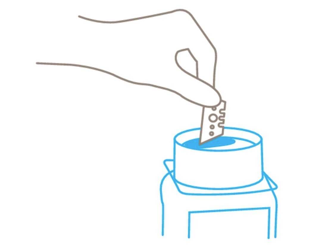 Une main trempe une lame de rasoir dans un liquide bleu dans un récipient.