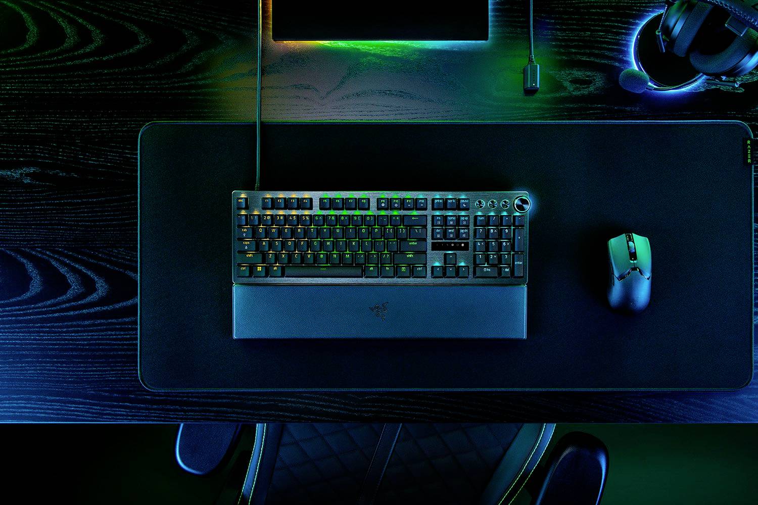 Un clavier et une souris rétroéclairés sur un bureau à surface en bois sombre. Des écouteurs sont posés en haut à droite.