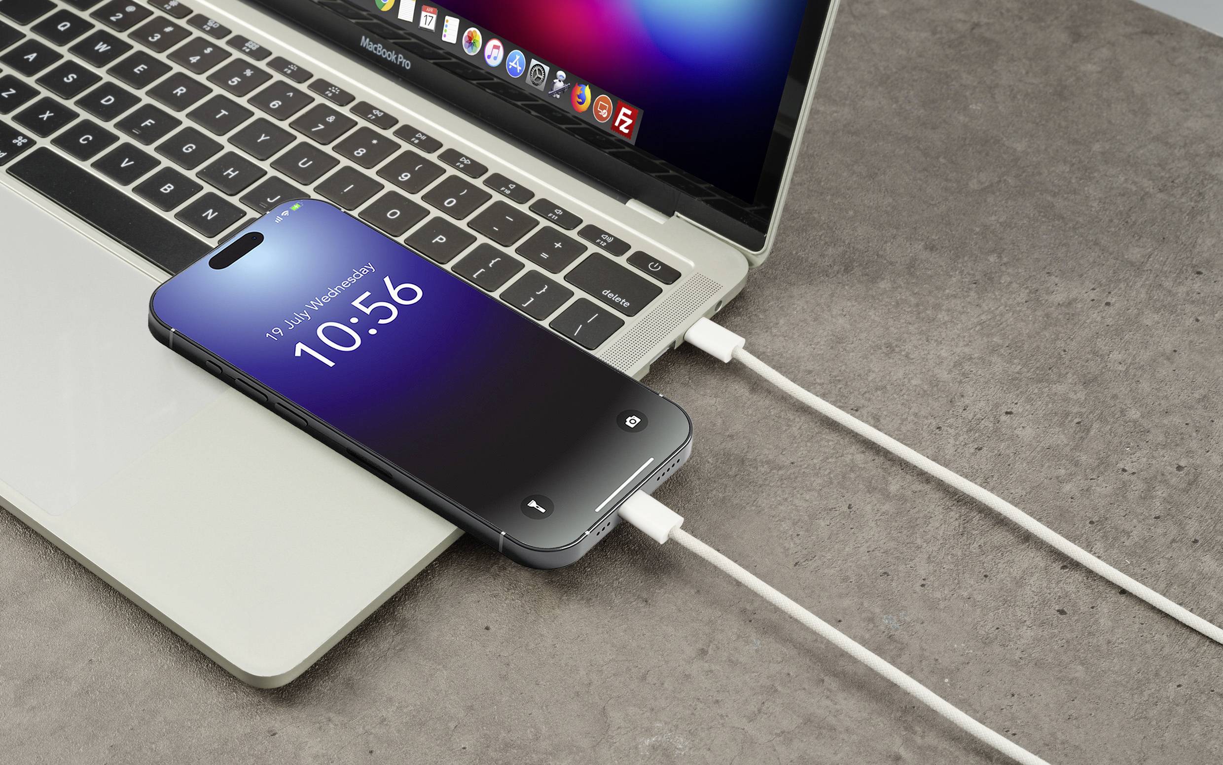 Un smartphone se charge via un câble connecté à un ordinateur portable. L'écran du smartphone affiche l'heure '10:56'.