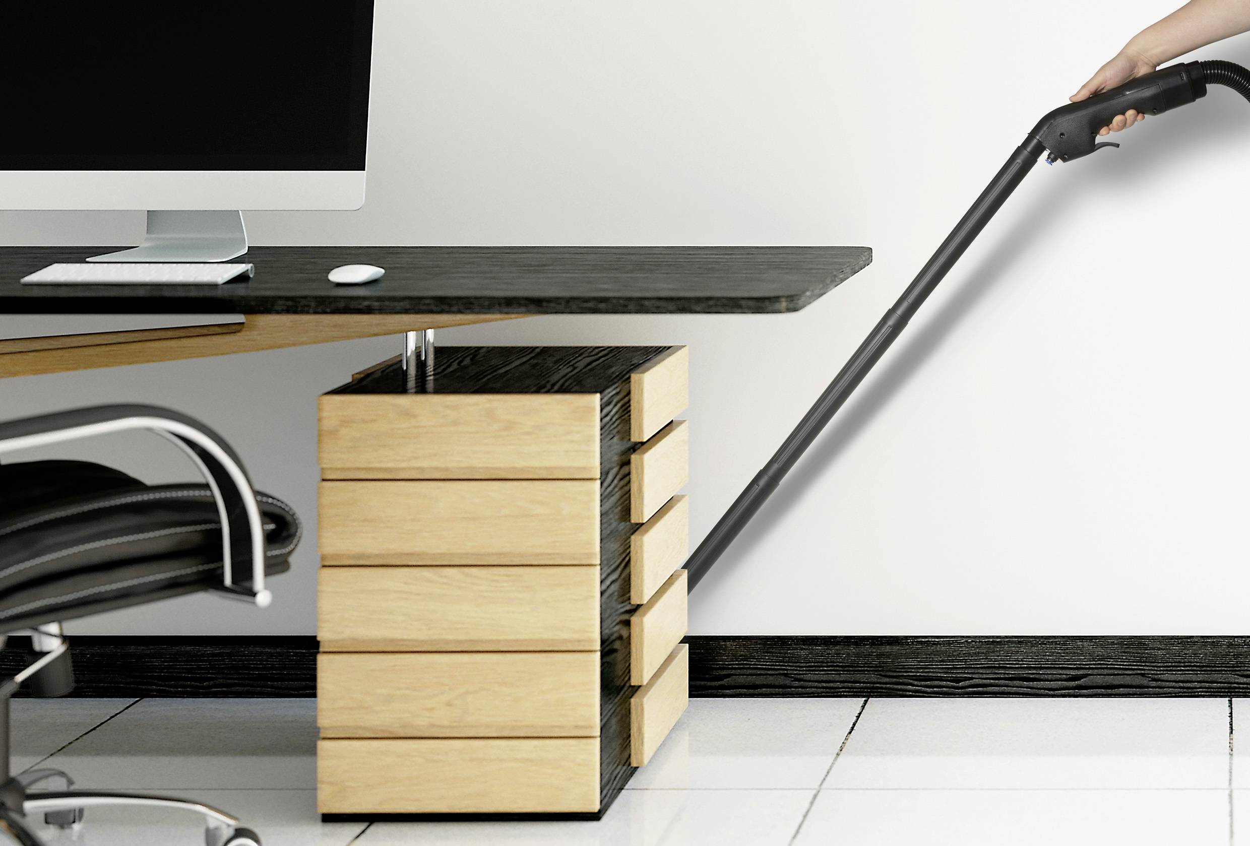 Une personne passe l'aspirateur sur le sol d'un espace de bureau moderne. Au premier plan, un bureau avec un ordinateur et un petit caisson de rangement.