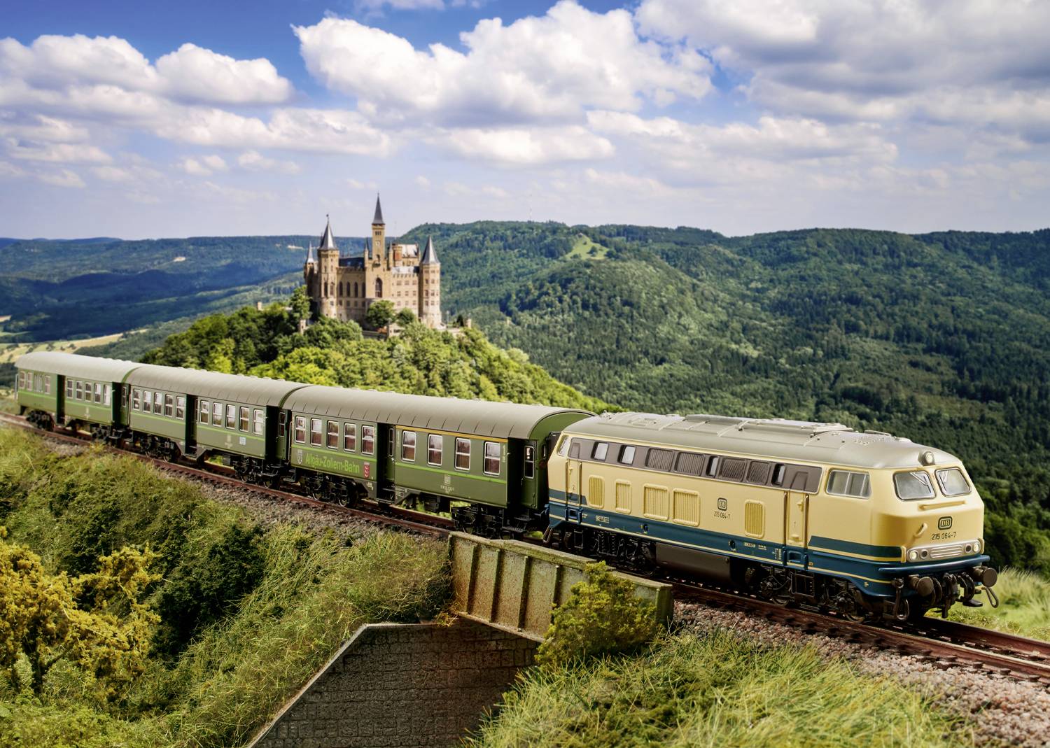 Un train traverse un paysage vallonné avec un château en arrière-plan et des collines boisées sous un ciel nuageux.