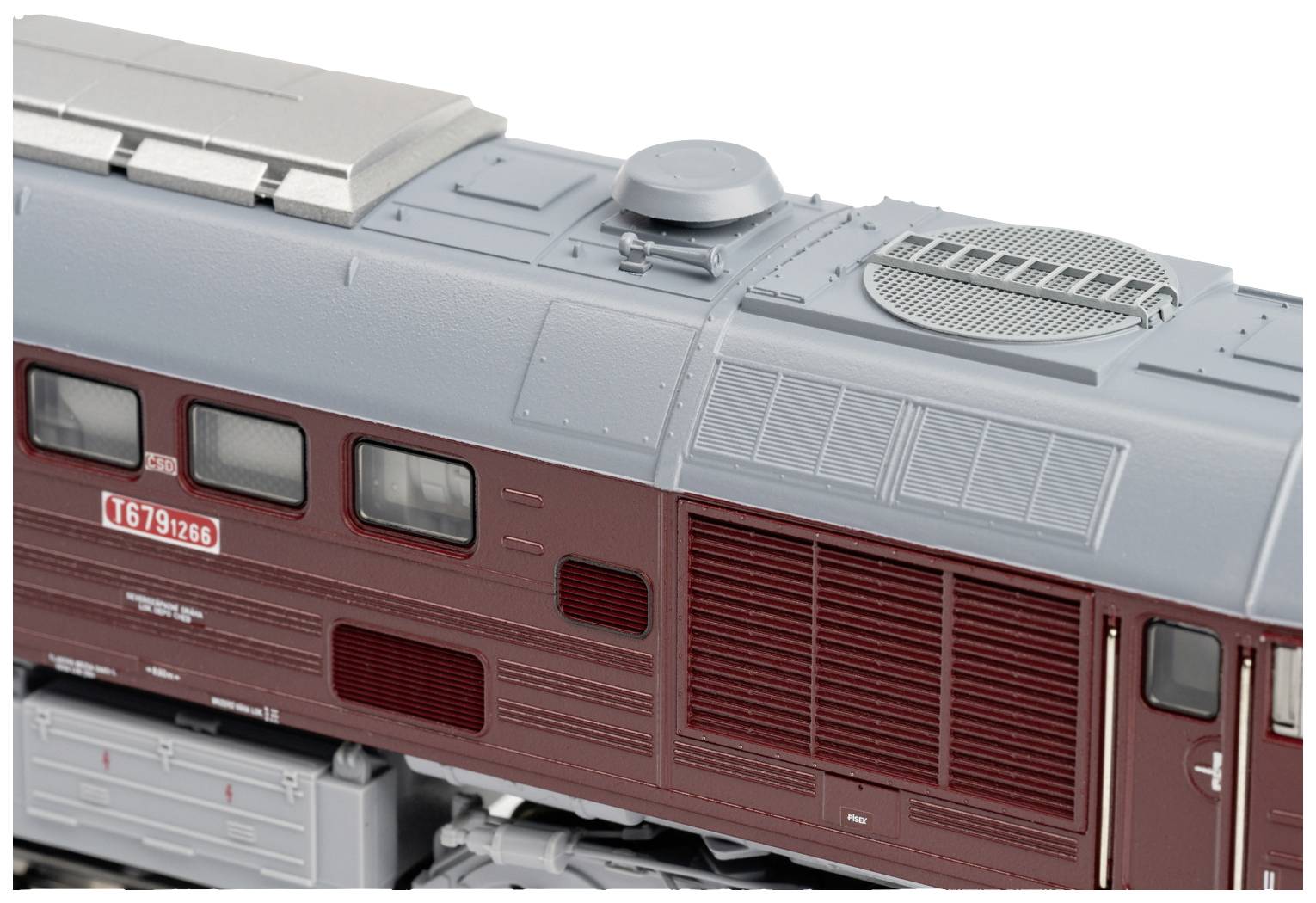 Gros plan d'un train miniature en rouge bordeaux et gris, avec des détails visibles tels que des grilles de ventilation, des fenêtres et l'inscription 'T679 976'.