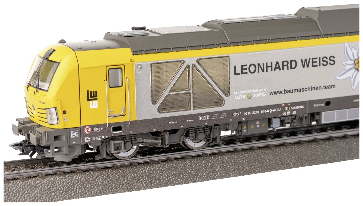 Locomotive électrique jaune et grise portant l'inscription 'LEONHARD WEISS', stationnée sur une voie ferrée.