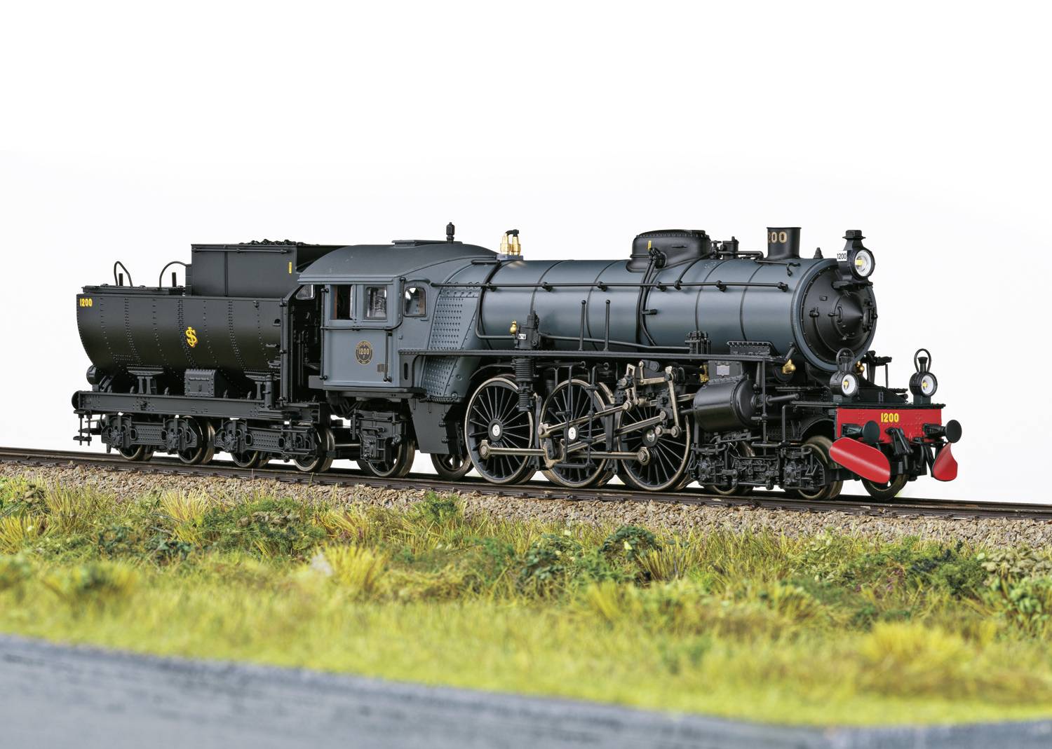 Modèle de locomotive à vapeur sur un rail, représenté en détail sur un fond blanc, entouré d'herbe. Locomotive en gris avec des détails rouges.