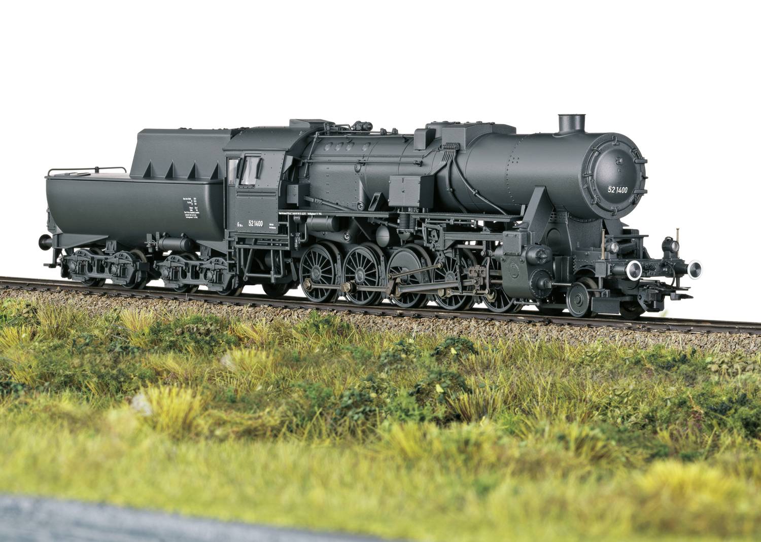 Locomotive miniature noire sur un rail, vue latérale, montrant des détails techniques précis. Talus ferroviaire couvert d'herbe au premier plan.