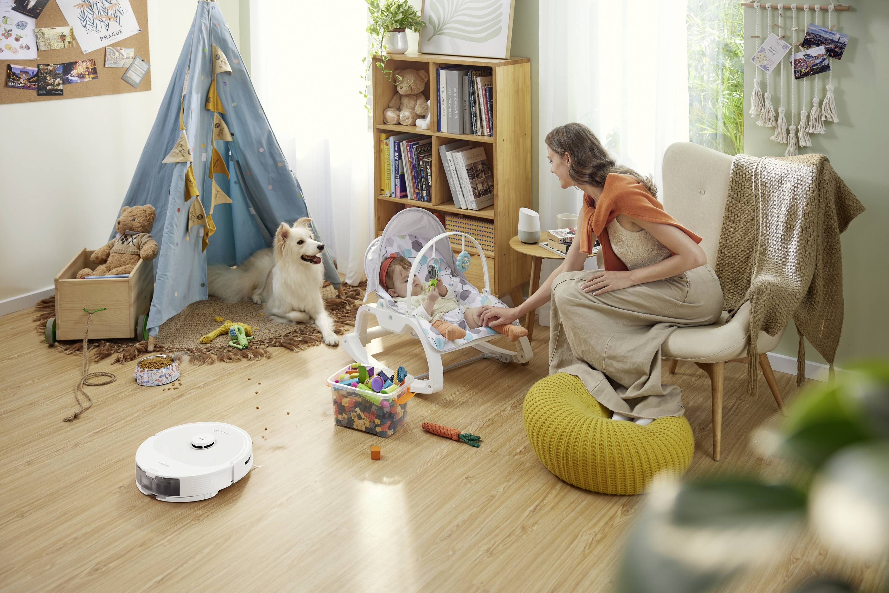 Une femme prend tendrement soin d'un bébé dans un transat dans la chambre d'enfant. Un chien est assis à côté d'un coffre rempli de jouets.