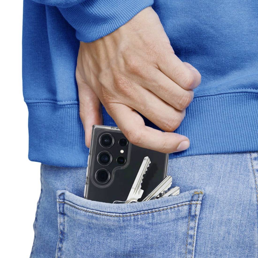 Une main glisse un smartphone et un trousseau de clés dans la poche arrière d'un jean. La personne porte un pull bleu.