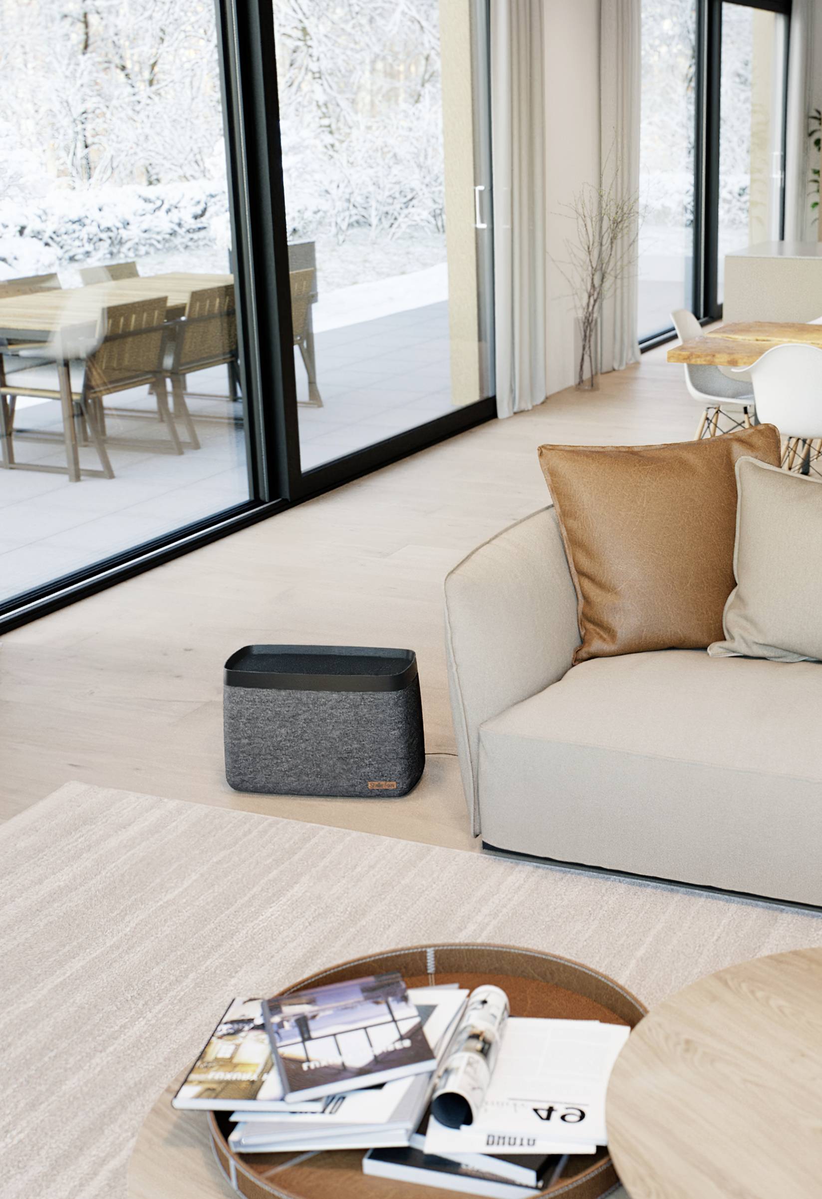 Salon moderne avec de grandes fenêtres donnant sur une terrasse enneigée. Un haut-parleur gris est placé à côté d'un canapé beige.