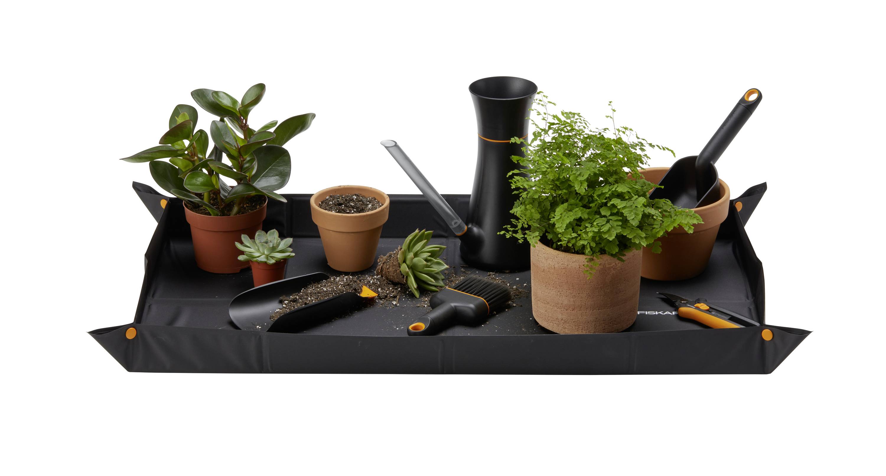 Un bac rectangulaire avec différents pots de fleurs, de la terre et deux outils de jardinage posés dessus.