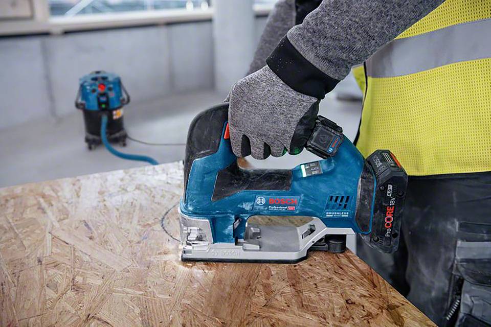 'Ouvrier utilisant une scie sauteuse pour couper une planche de bois dans un environnement d'atelier.'