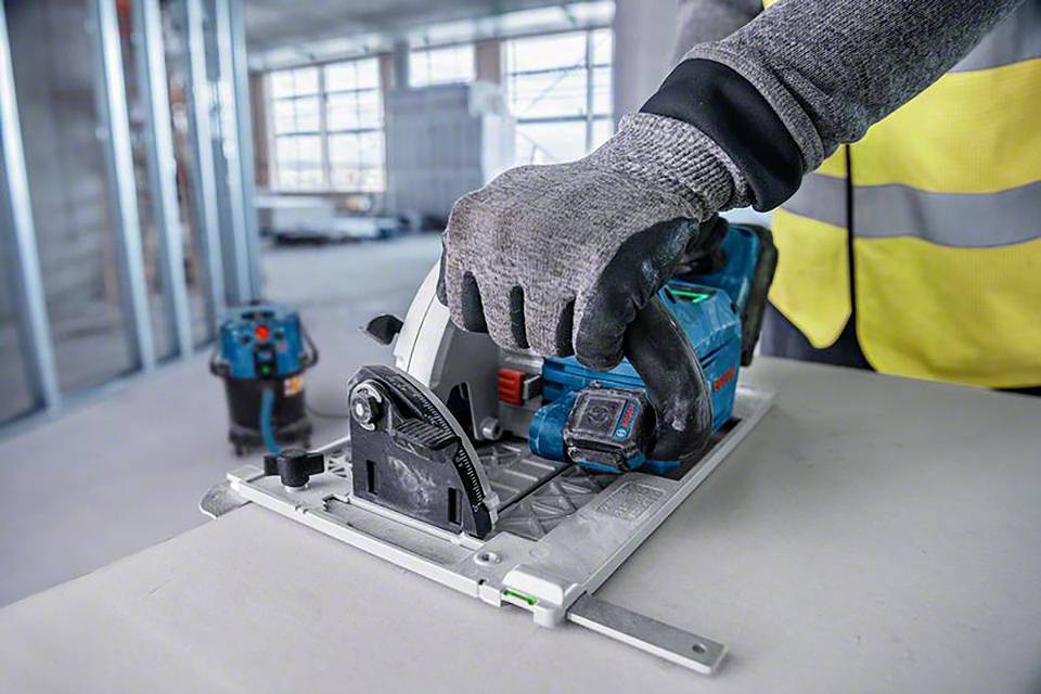 Un ouvrier utilise une scie circulaire manuelle sur un chantier, portant des vêtements de sécurité et des gants ; l'accent est mis sur la sécurité et la précision.