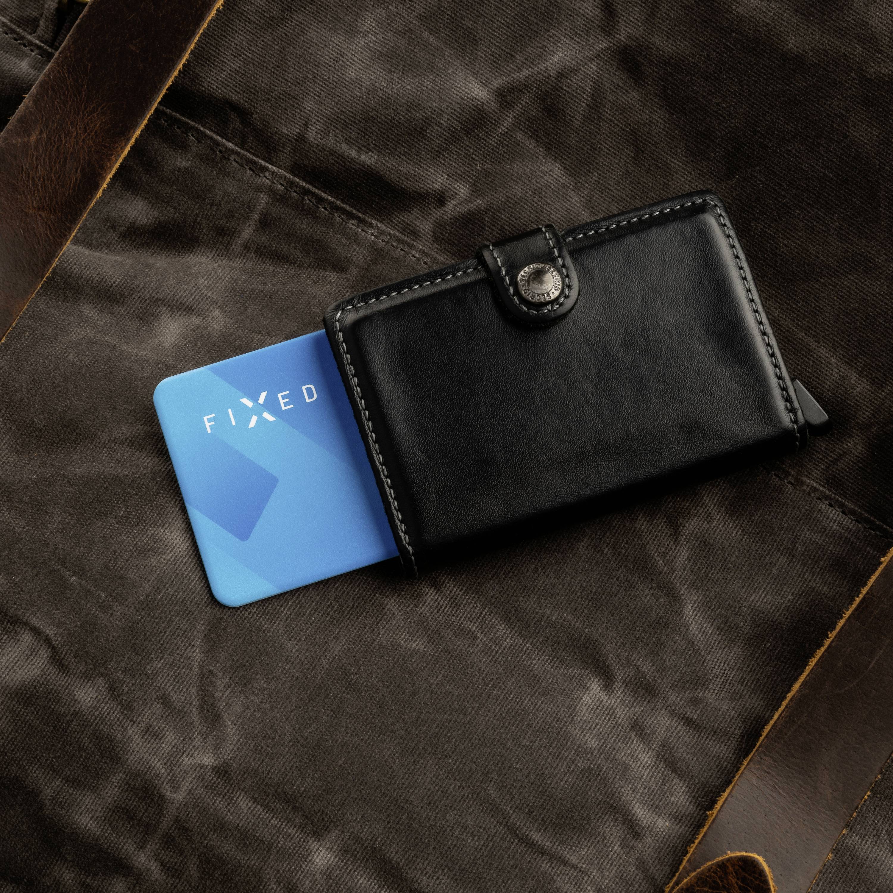 Un portefeuille en cuir noir est posé sur un fond de tissu marron, à côté se trouve une carte bleue portant l'inscription 'FIXED'.