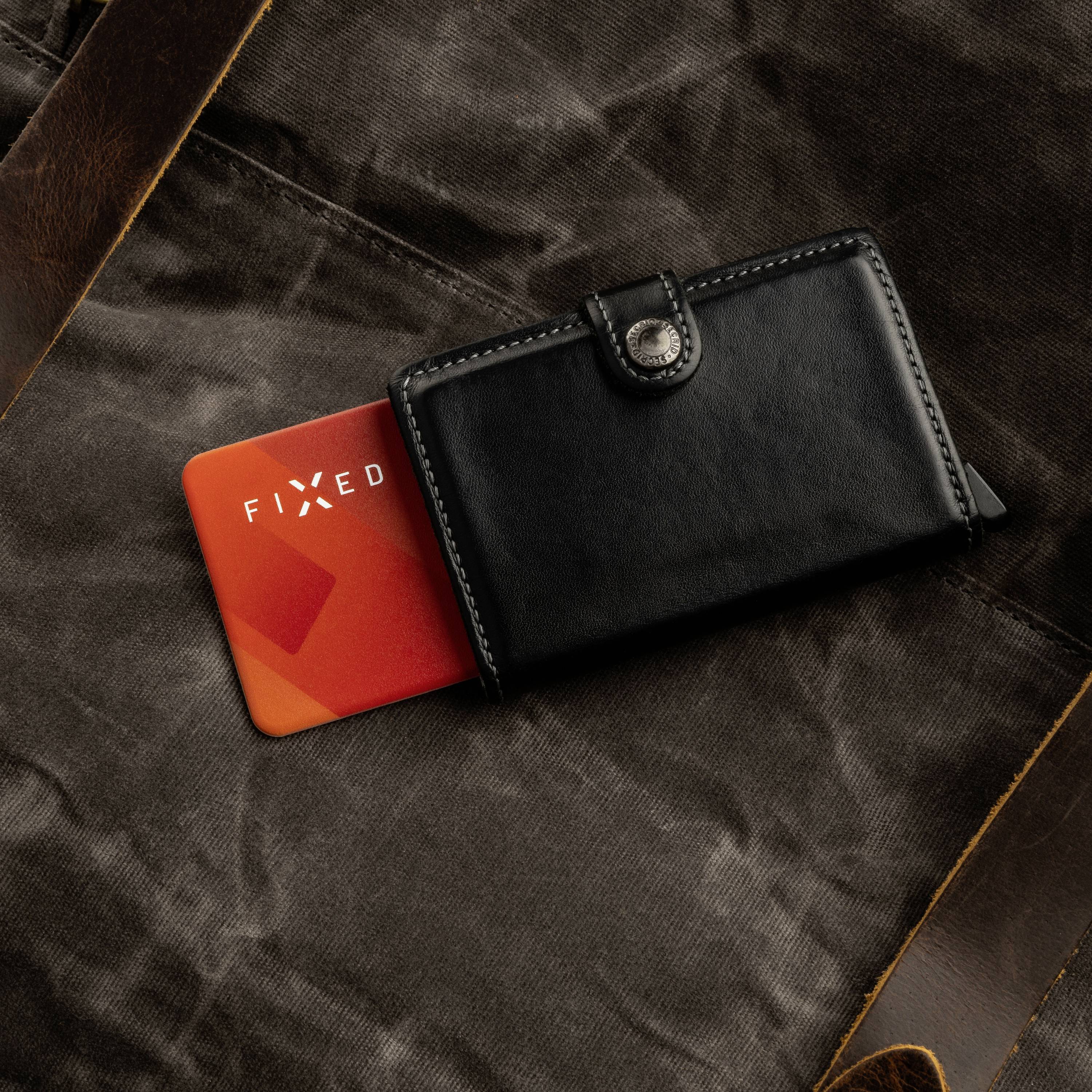 Portefeuille noir en cuir avec une carte rouge partiellement sortante, portant l'inscription 'FIXED', sur un fond de tissu marron.