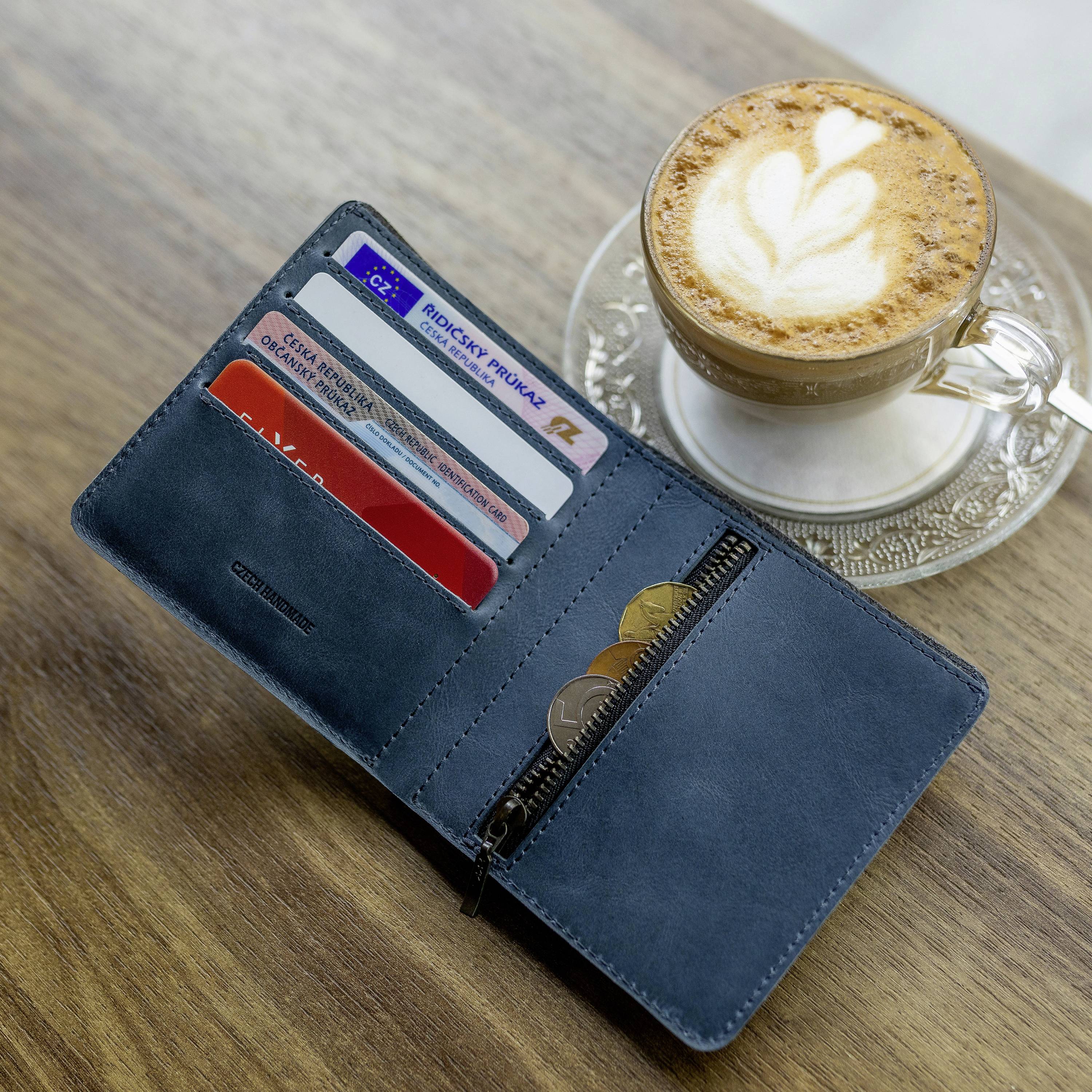 Un portefeuille bleu ouvert contenant des cartes de crédit et des pièces de monnaie est posé sur une surface en bois. À côté se trouve une tasse de cappuccino.