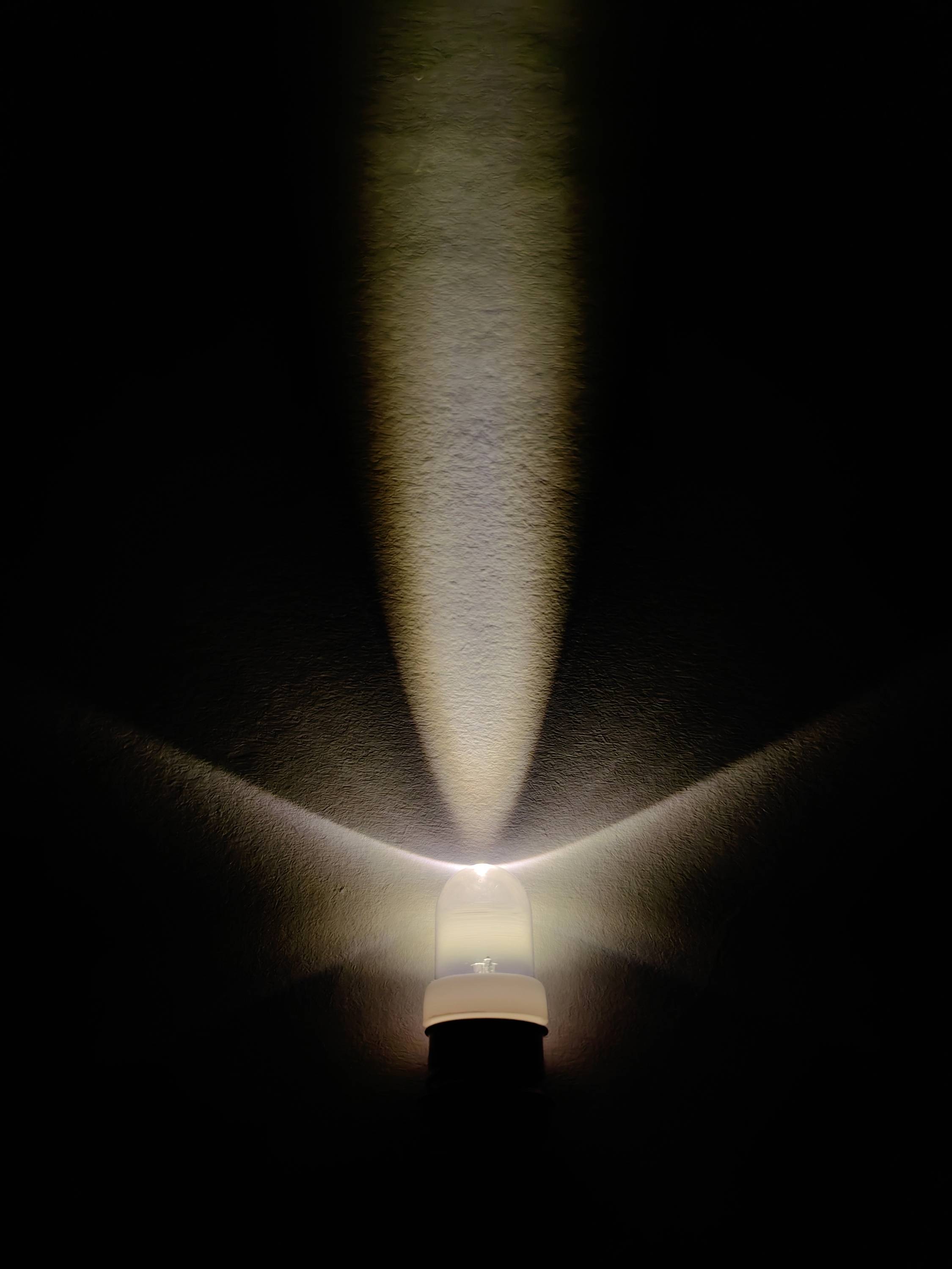 Une ampoule brille dans une pièce sombre et crée un motif lumineux en forme de rayons sur le mur.