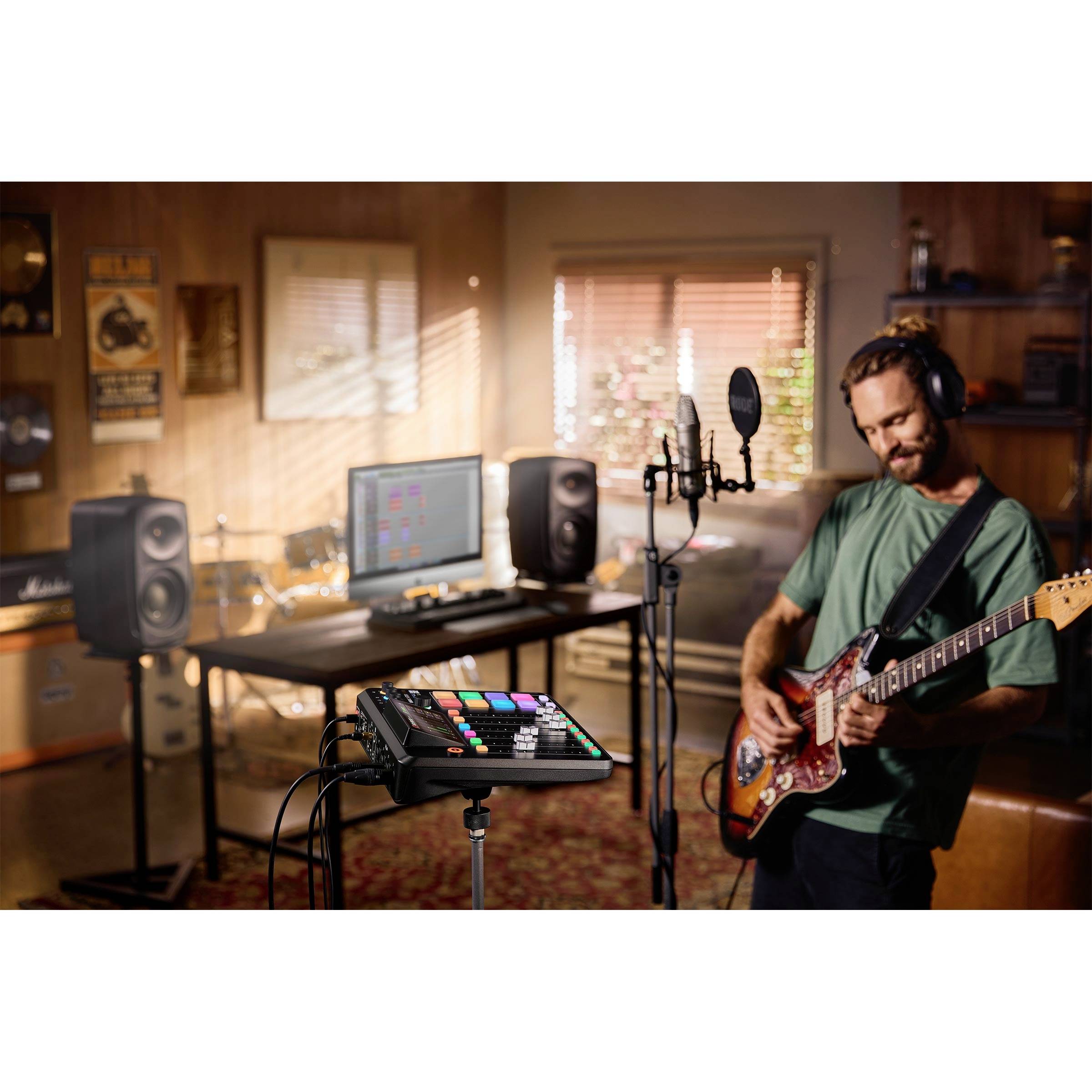 Un homme joue de la guitare dans un home studio. Un microphone est placé devant lui, et en arrière-plan se trouve un bureau avec des écrans et des enceintes.