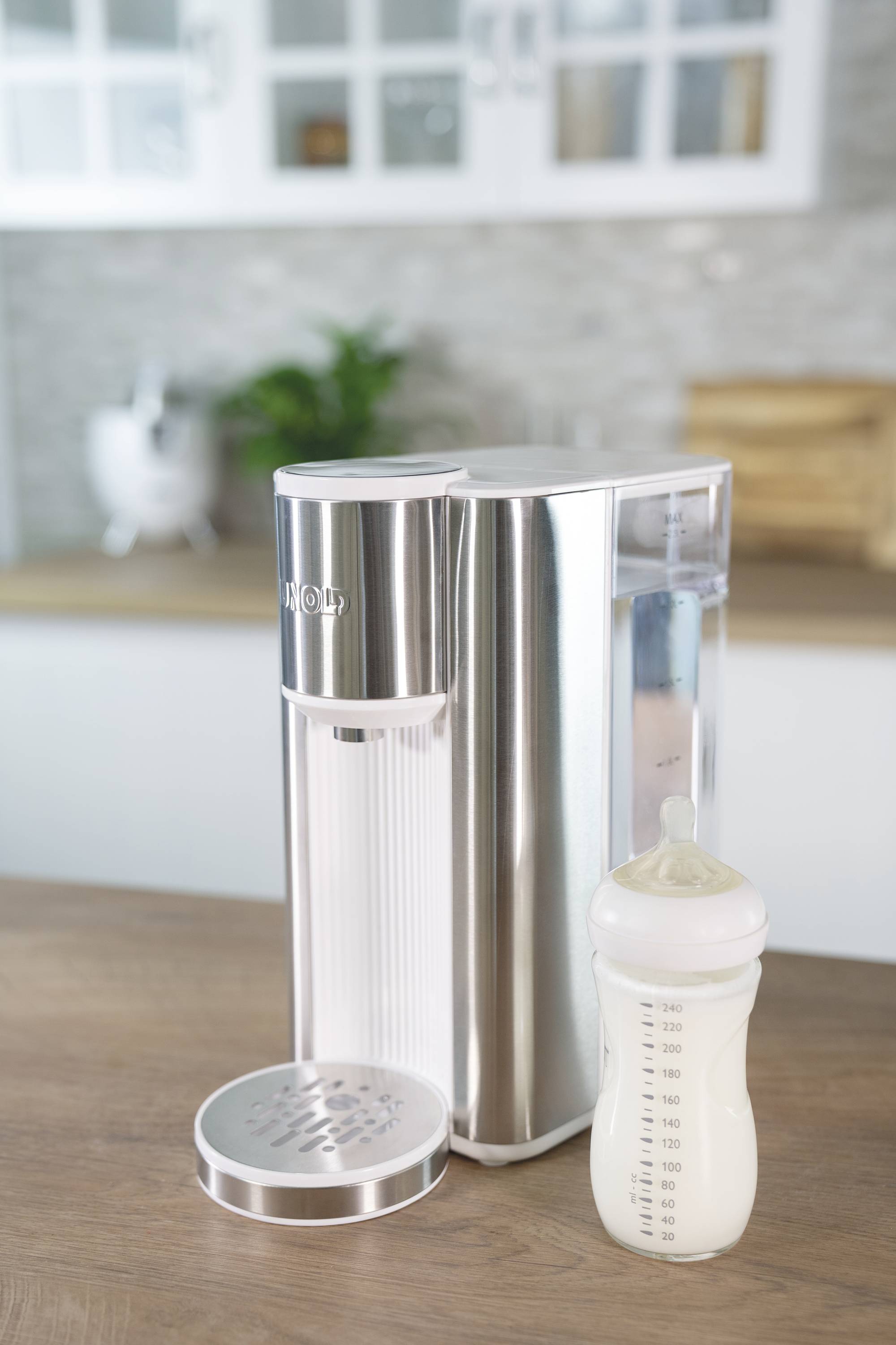 Un tire-lait posé sur un plan de travail de cuisine à côté d'un biberon de lait, avec des éléments de cuisine flous en arrière-plan.