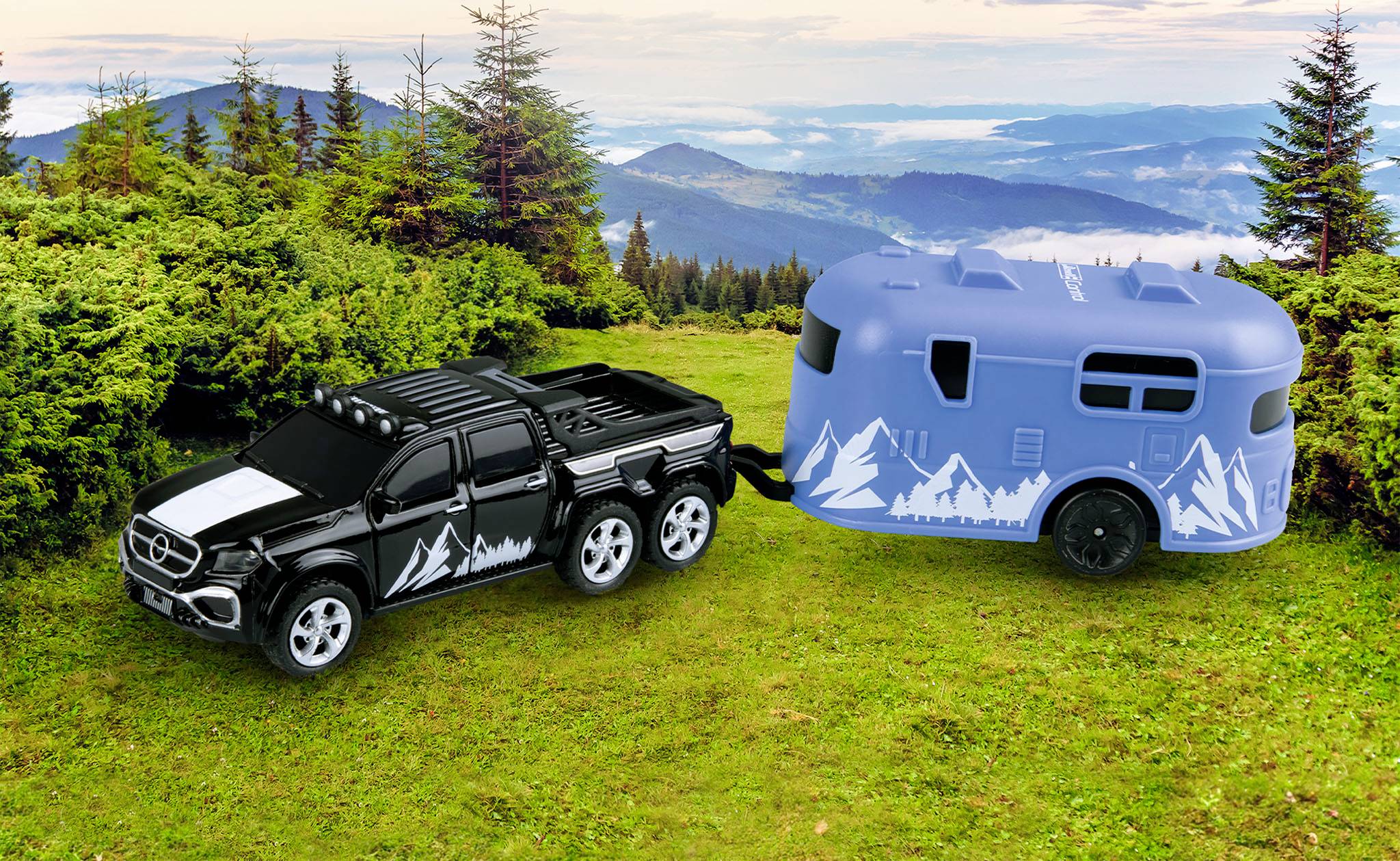 Une petite voiture jouet noire à six roues tractant une caravane bleue décorée de motifs montagneux, traversant un paysage herbeux avec un fond de montagnes.
