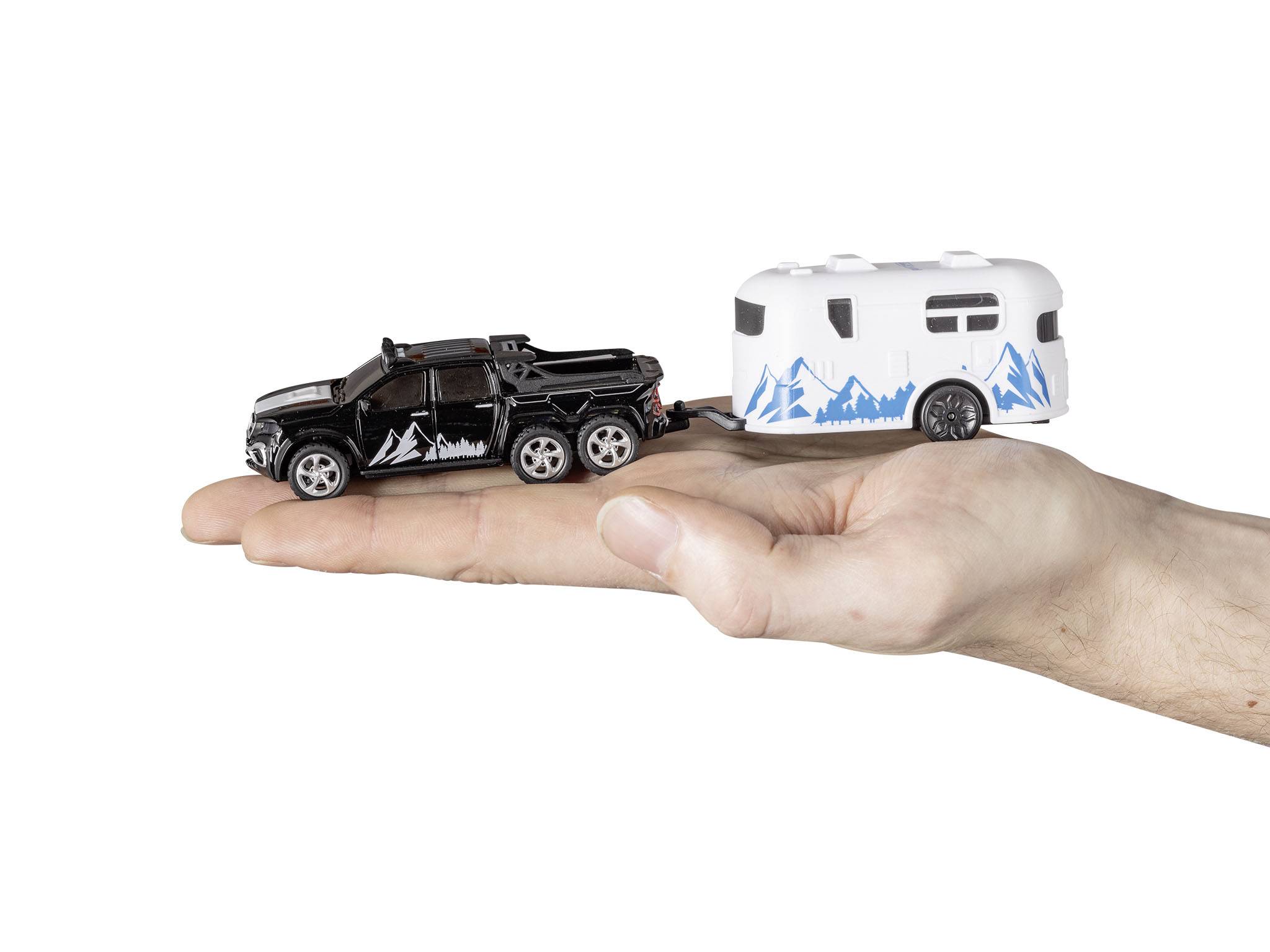 Un camion-jouet à remorque à six roues de style montagnard est posé sur une main tendue. La remorque est blanche avec des motifs bleus.