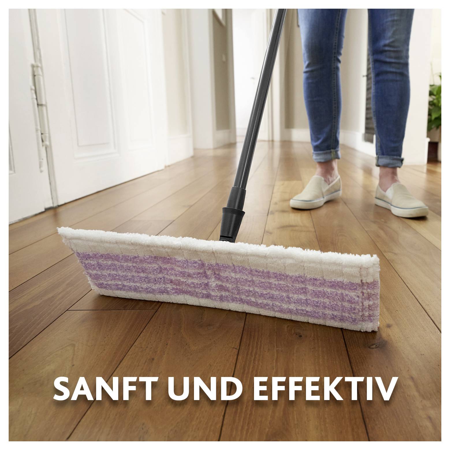 Balai avec un pad violet et blanc sur un plancher en bois à côté d'une personne en jeans et pantoufles; le texte dit 'DOUX ET EFFICACE'.