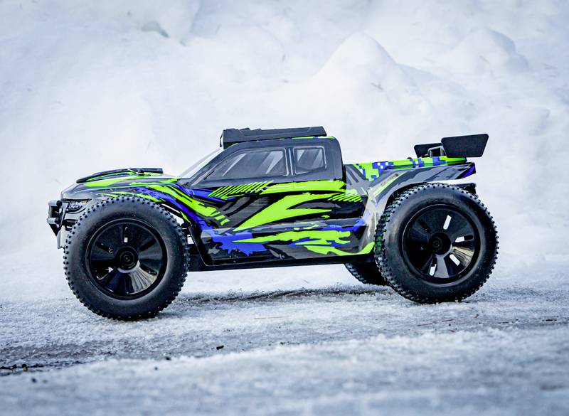 Une voiture télécommandée avec des motifs verts et bleus est posée sur un sol enneigé.