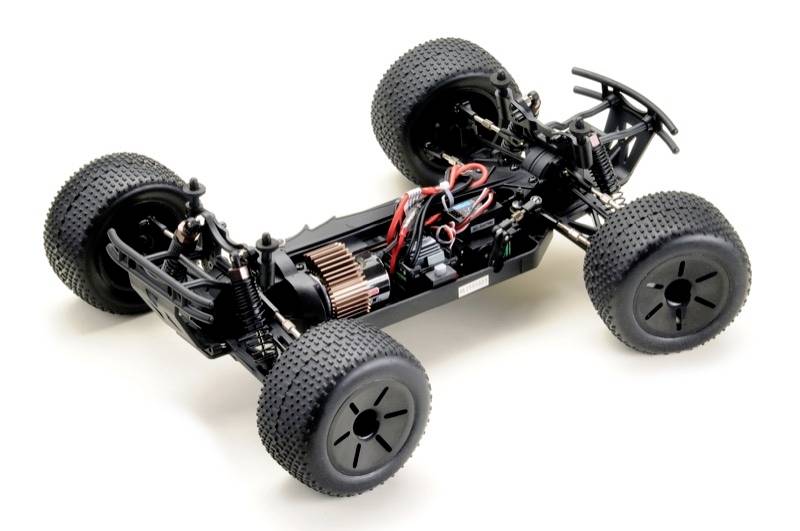 Châssis de voiture télécommandé avec de grandes roues striées, moteur et câbles visibles sur un fond clair.