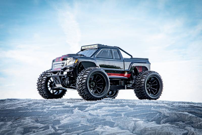 Véhicule tout-terrain miniature avec de grandes roues et des touches noires et rouges, posé sur une surface gelée et glacée sous un ciel bleu.