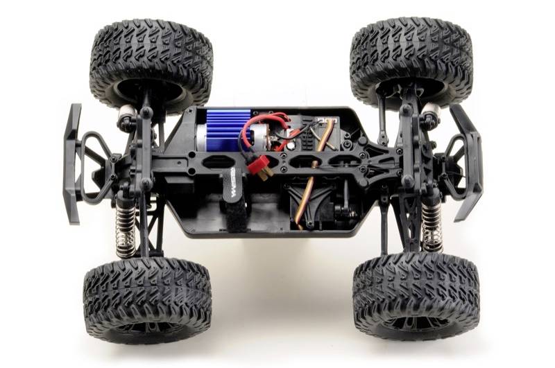 Châssis de voiture télécommandé avec des roues, une suspension et des composants électriques visibles, photographié sur un fond blanc.