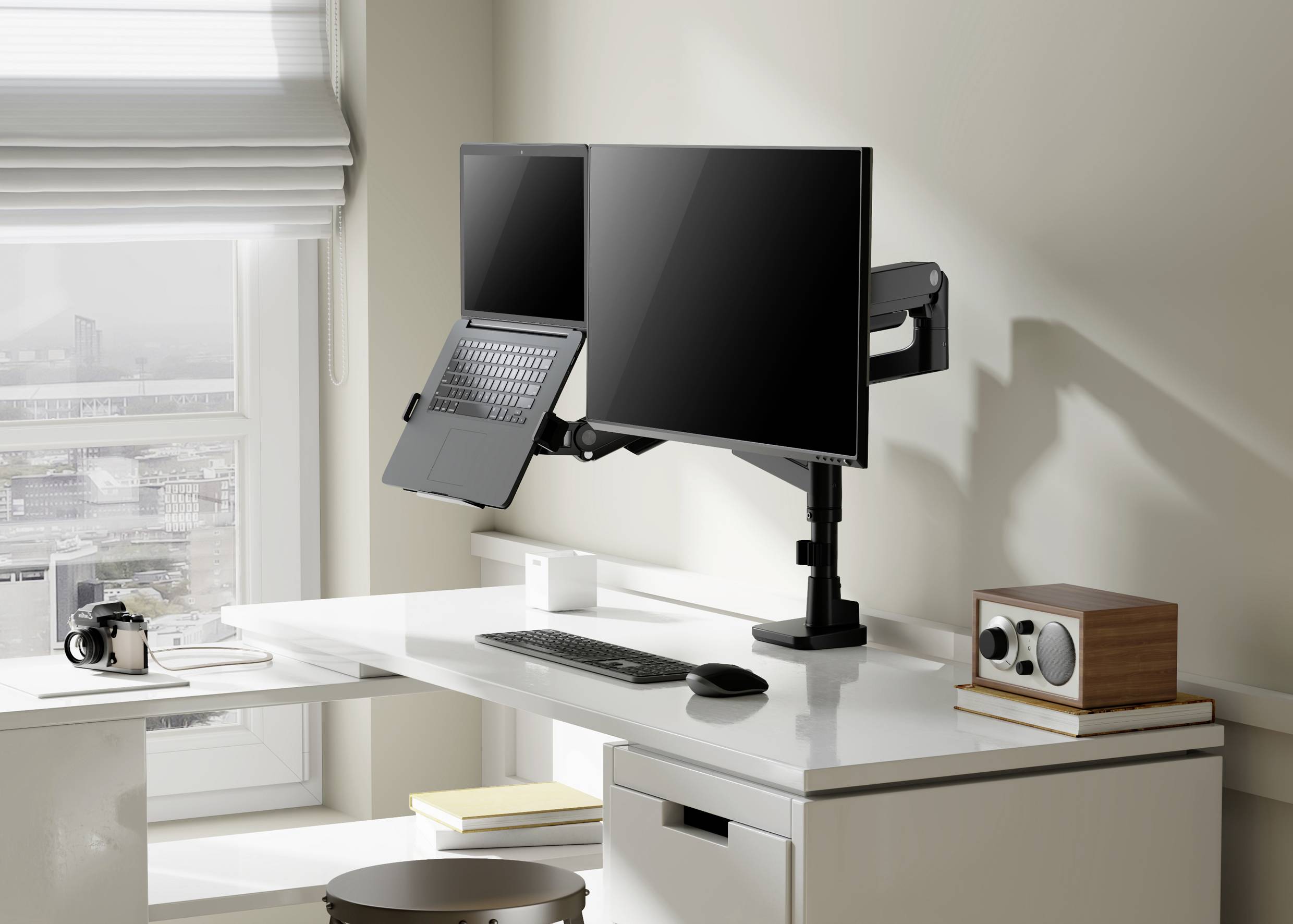 Un bureau moderne et bien rangé avec deux écrans, un ordinateur portable, un clavier, une souris et une caméra près de la fenêtre.