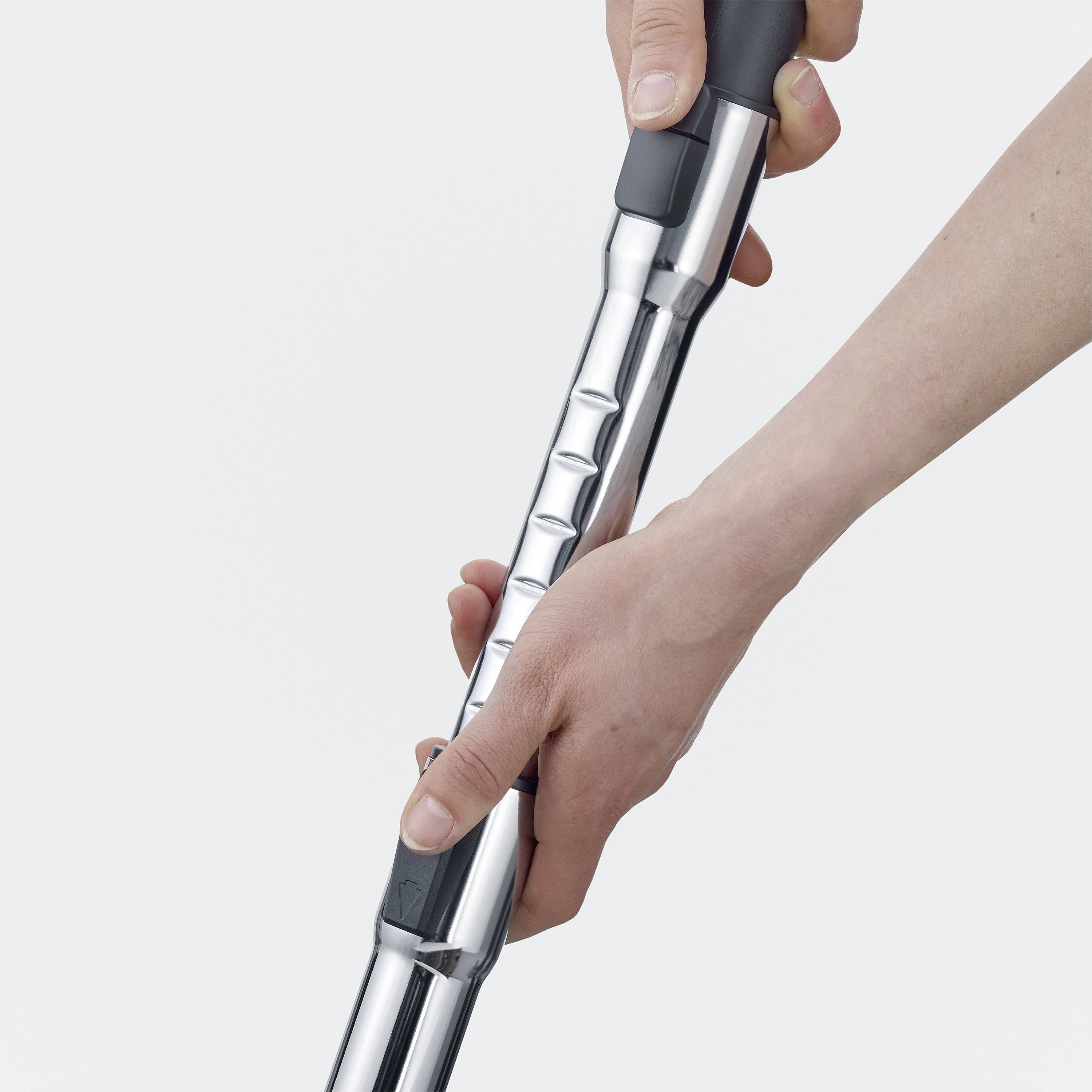 Une personne tient un aspirateur élégant avec un tube métallique brillant. L'image se concentre sur la main et la poignée.