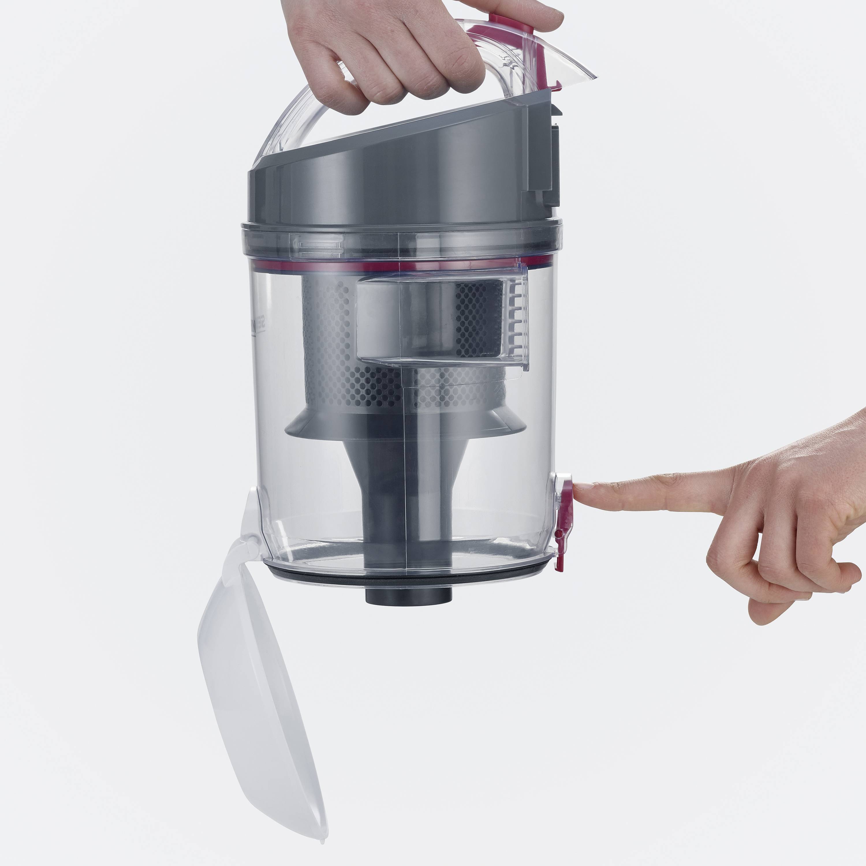 Un conteneur d'aspirateur est tenu par une main, tandis qu'une autre main ouvre le couvercle. Le récipient est transparent.
