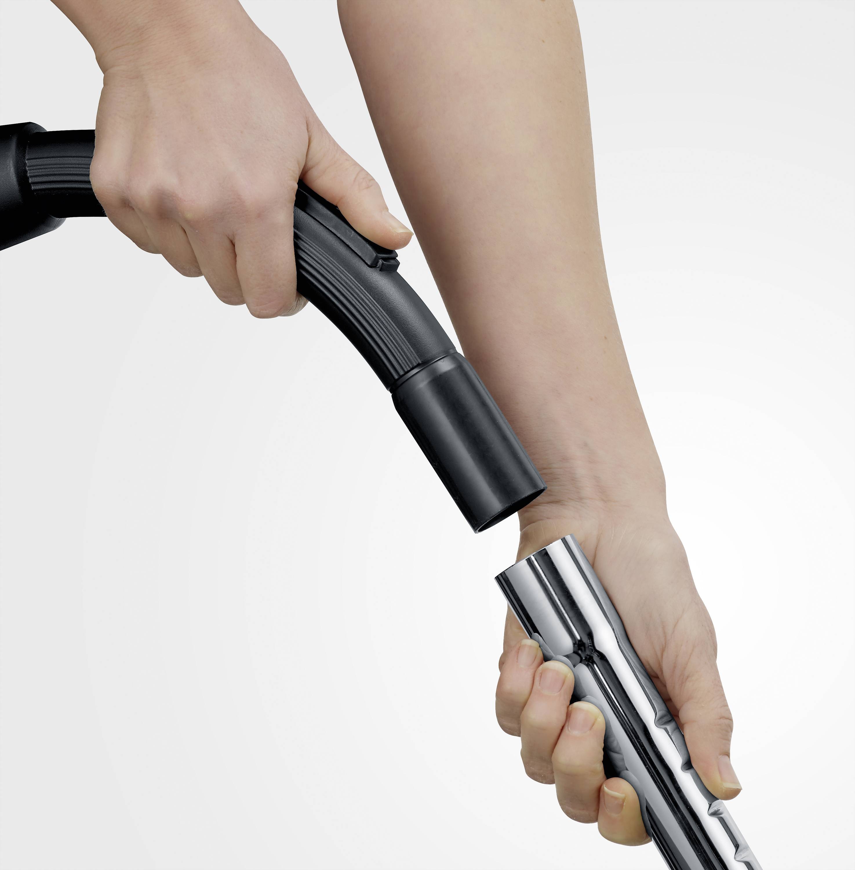Une personne tient un tuyau d'aspirateur et le raccorde à un tube métallique. Manipulation pratique d'un appareil électroménager.