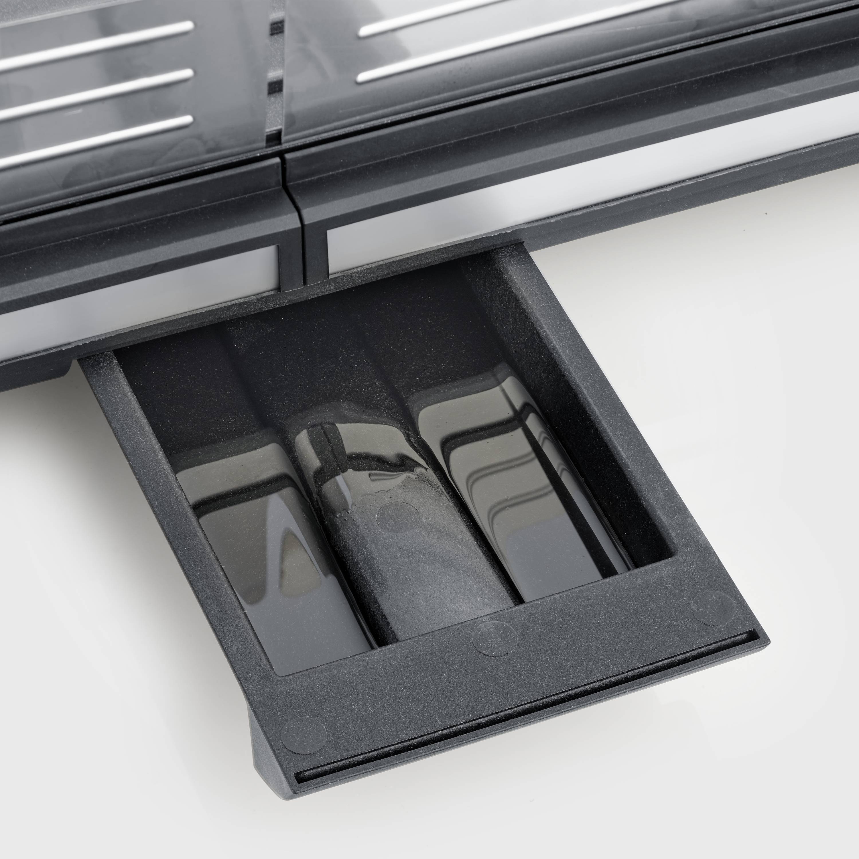 Un bac noir et coulissant sous un appareil gris, probablement un grille-pain. Le bac semble être amovible.