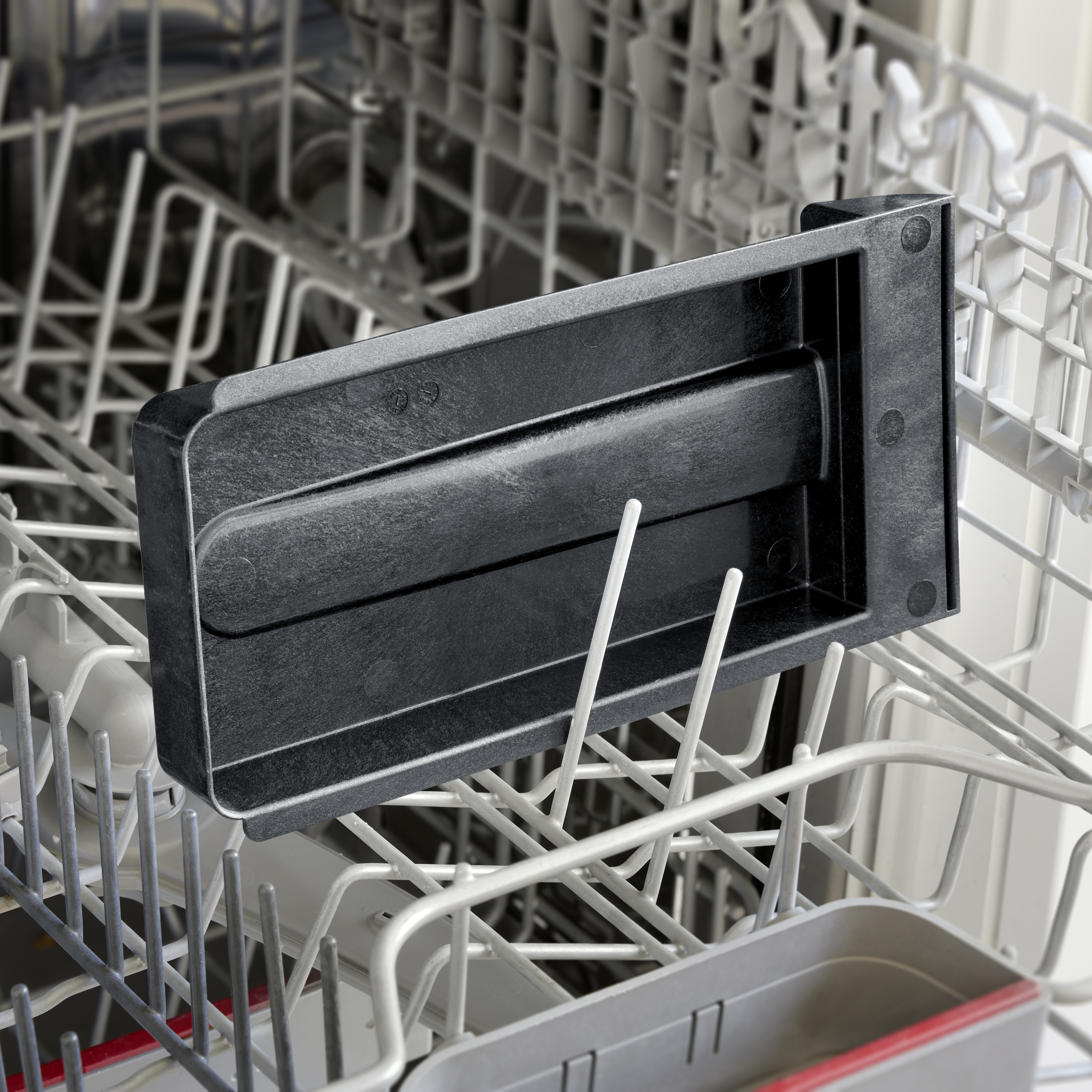 Un objet en plastique noir placé dans le fond du lave-vaisselle ouvert. Il se distingue par un design simple.